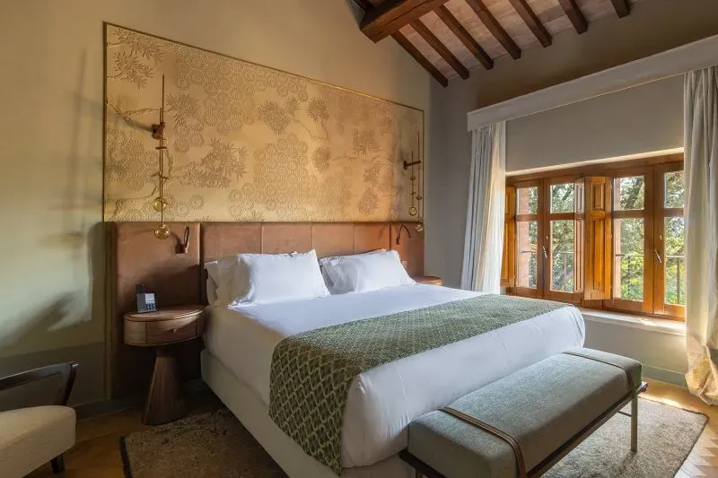 غرفة نوم أنيقة داخل منتجع زراعي، تحتوي على سرير مزدوج مع مفروشات مريحة ونوافذ كبيرة تطل على المناظر الطبيعية.