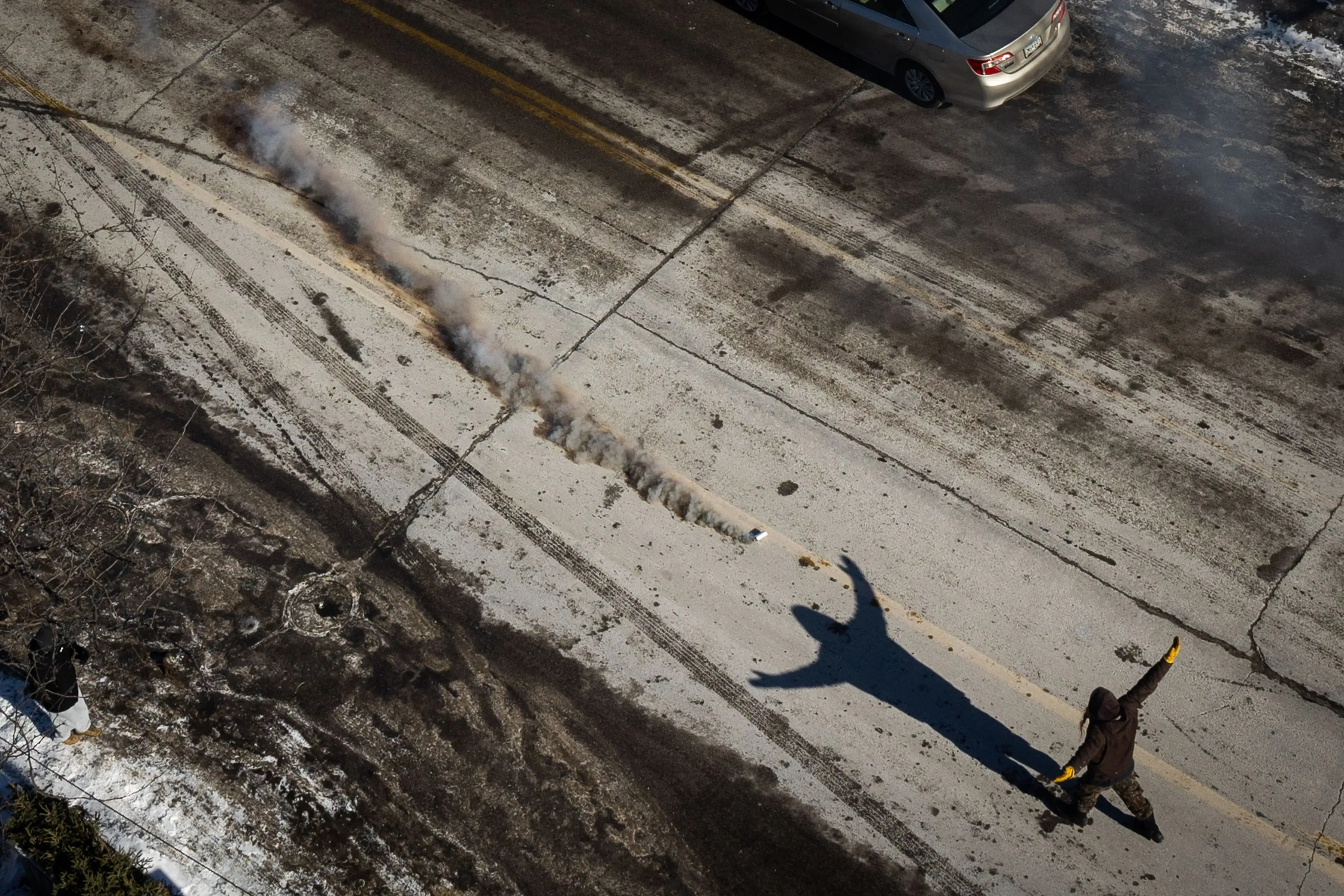 شخص يرتدي ملابس داكنة ويستخدم قنبلة دخانية في احتجاج على الطريق، مع وجود سيارات في الخلفية، مما يعكس التوترات الاجتماعية والسياسية.