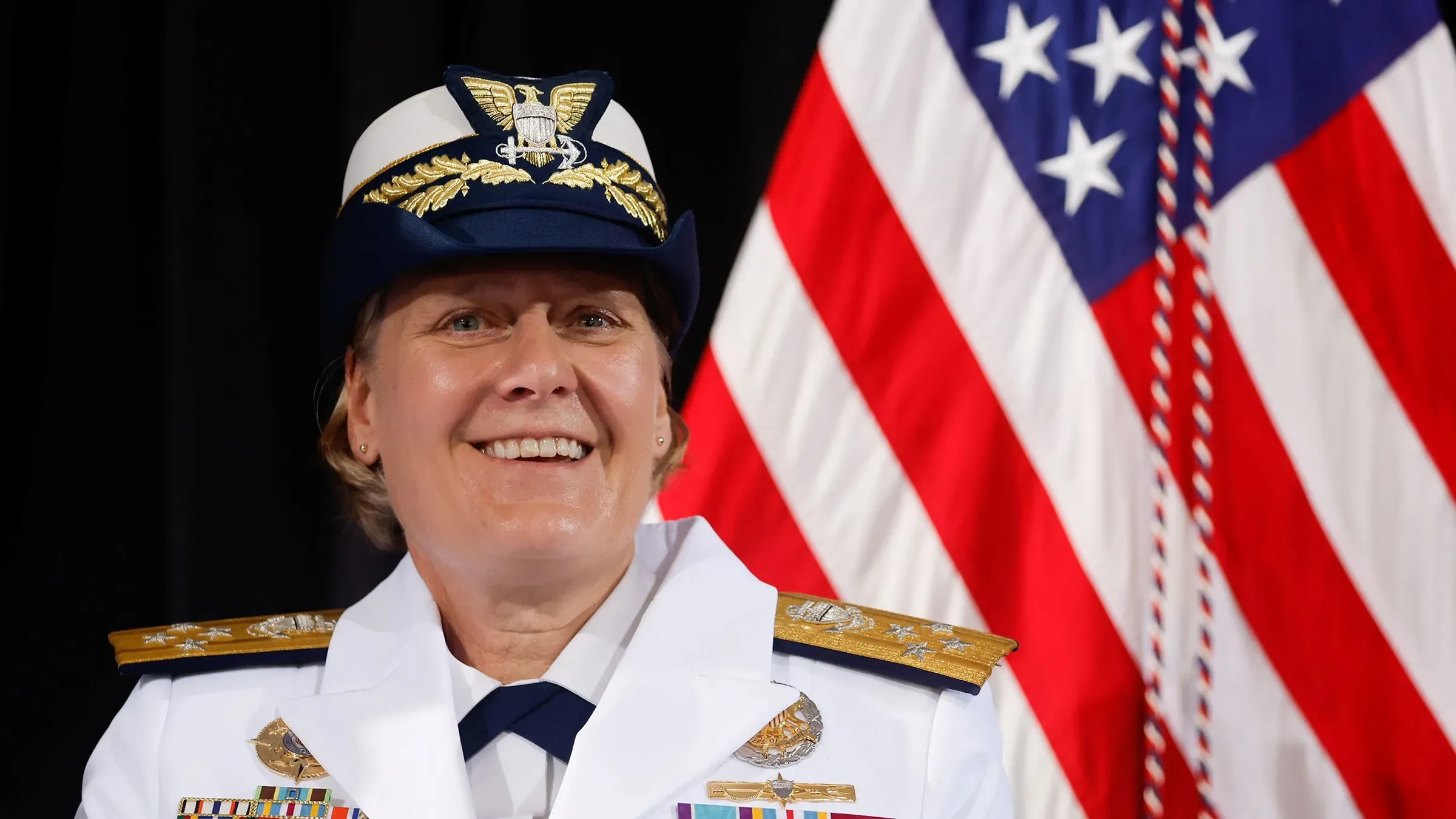 أدميرال ليندا فاغان مبتسمة في زيها الرسمي، مع العلم الأمريكي خلفها، بعد إقالتها من قيادة خفر السواحل بسبب أوجه قصور في القيادة.