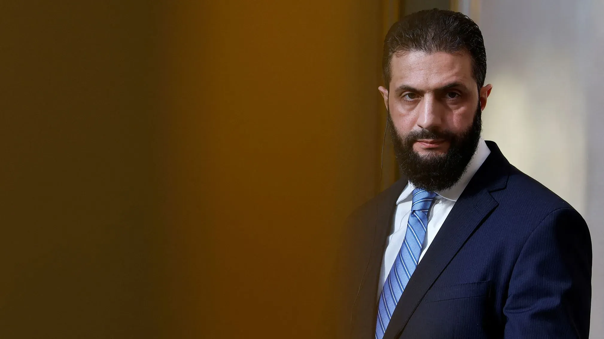 أحمد الشرع، قائد هيئة تحرير الشام، يظهر في مؤتمر صحفي، مع خلفية ضبابية، في سياق التغيرات السياسية في سوريا.