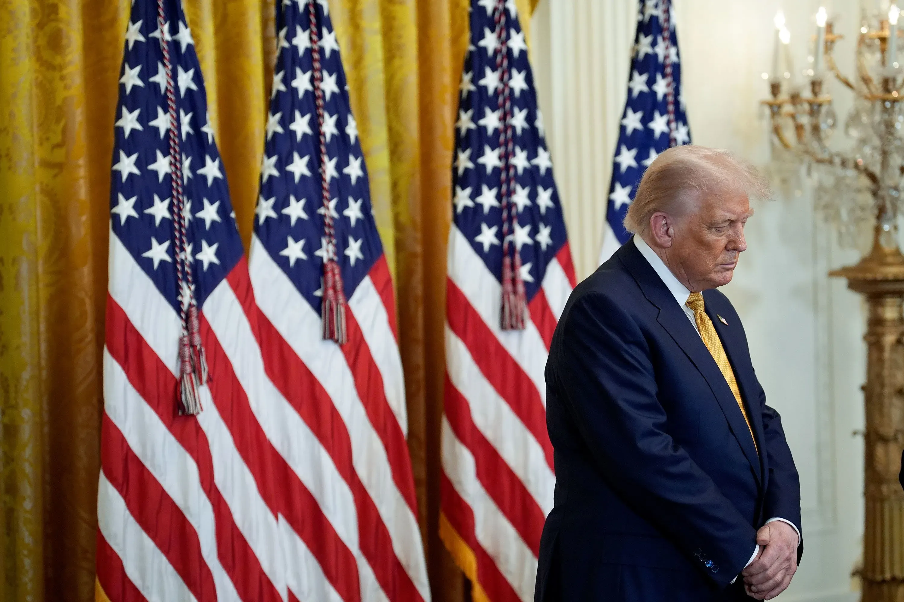 ترامب يقف بجوار أعلام الولايات المتحدة في غرفة رسمية، معبرًا عن التركيز على القضايا الدينية في مكان العمل الفيدرالي.