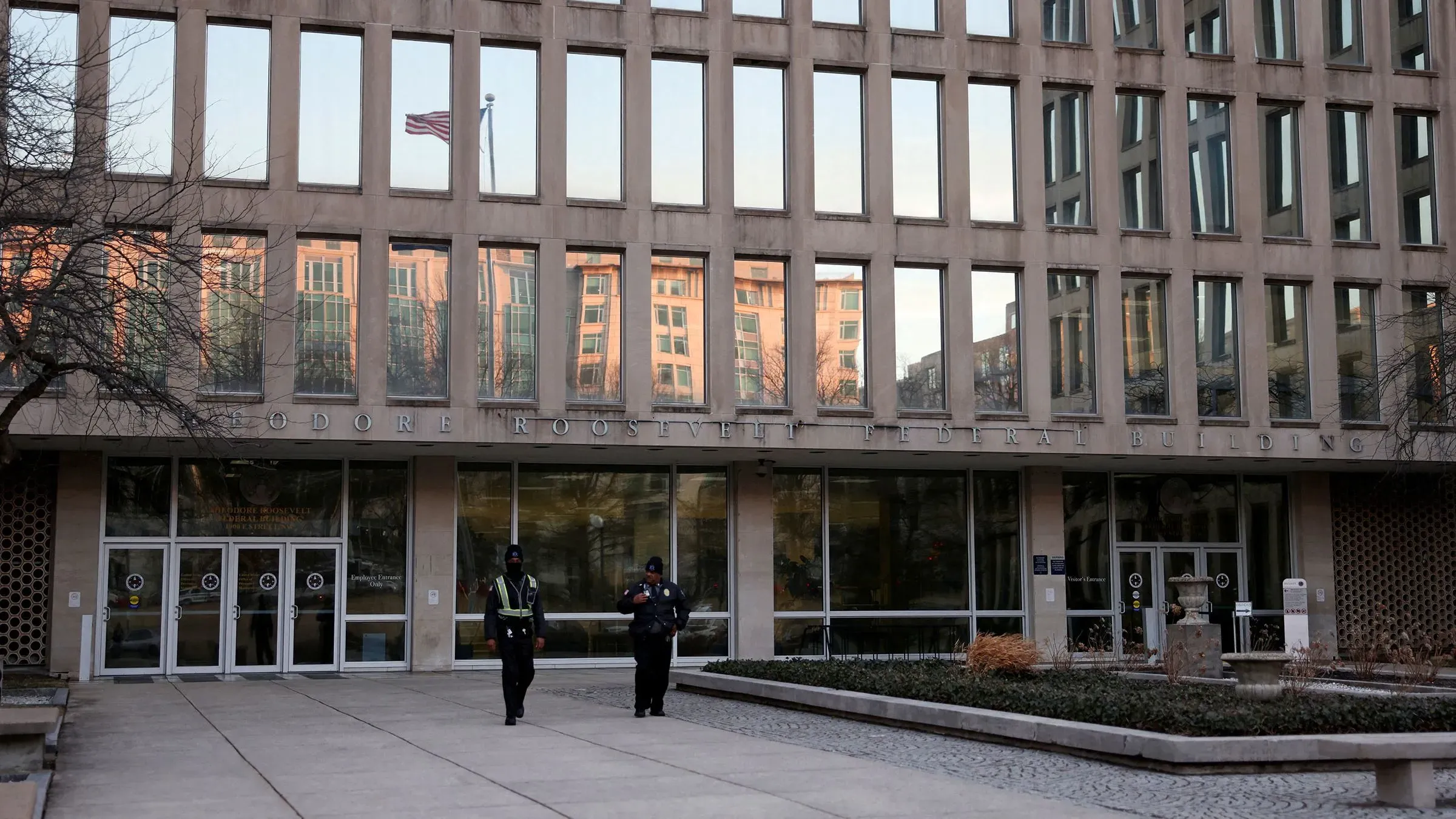 مدخل مبنى ثيودور روزفلت الفيدرالي، يظهر حراس أمن أمامه، مع العلم الأمريكي يرفرف في الخلفية، يعكس التوجهات الجديدة في التوظيف الفيدرالي.