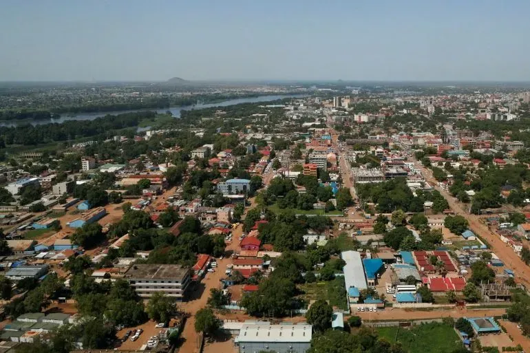 منظر جوي لمدينة جوبا في جنوب السودان، يظهر المباني والطرق والأشجار، مع نهر يمر عبر المنطقة، مما يعكس الأوضاع الحالية في البلاد.