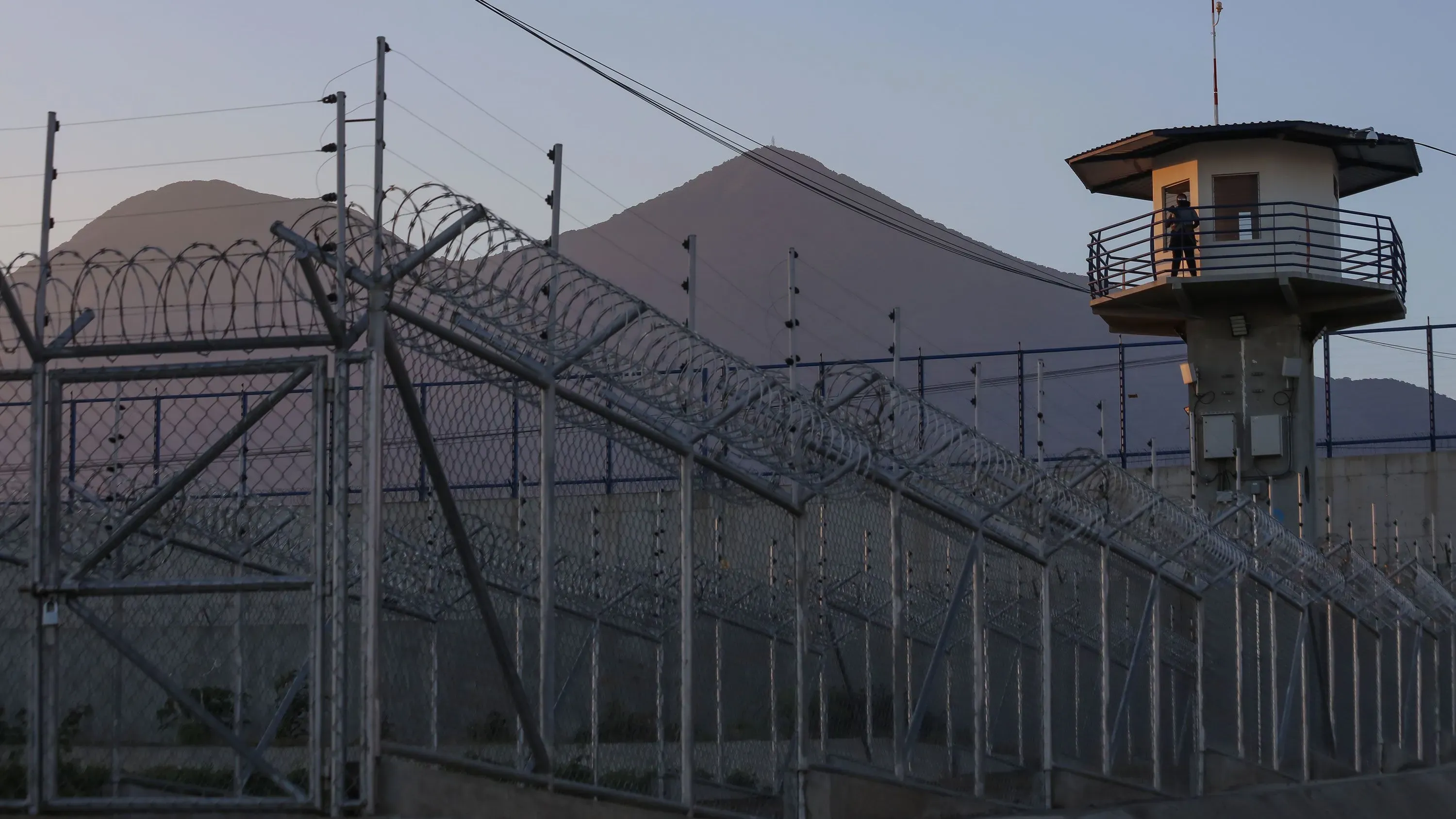 برج حراسة في سجن شديد الحراسة بالسلفادور محاط بسياج شائك، مع خلفية للجبال، في سياق عملية تبادل السجناء مع فنزويلا.