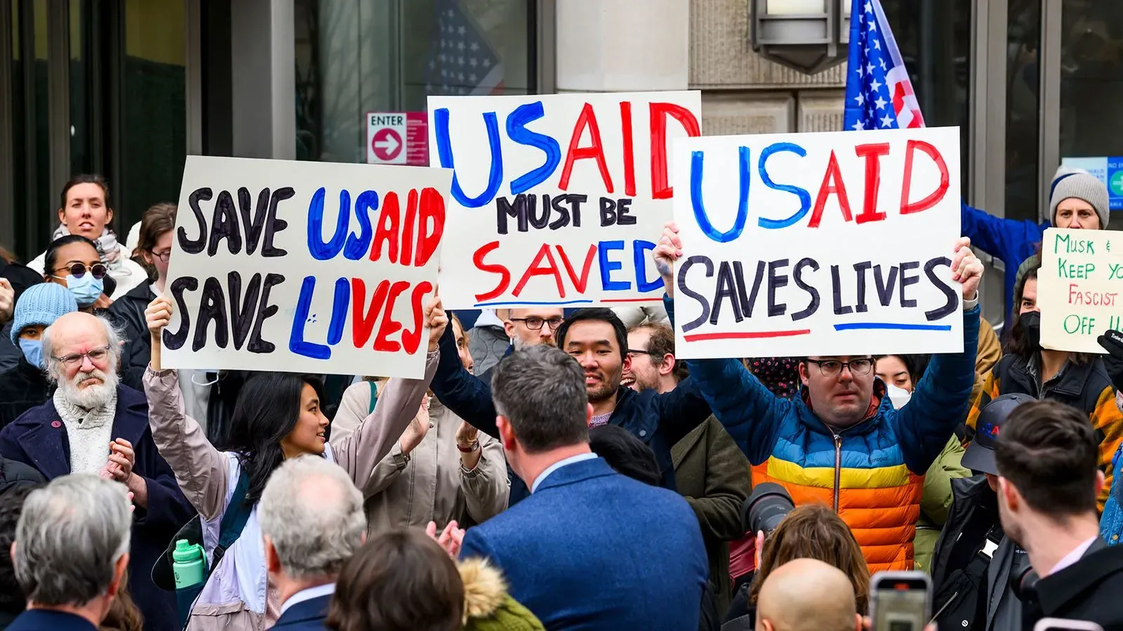احتجاجات أمام مبنى حكومي، حيث يحمل المتظاهرون لافتات تطالب بإنقاذ وكالة التنمية الدولية الأمريكية (USAID) ودعم حقوق الإنسان.