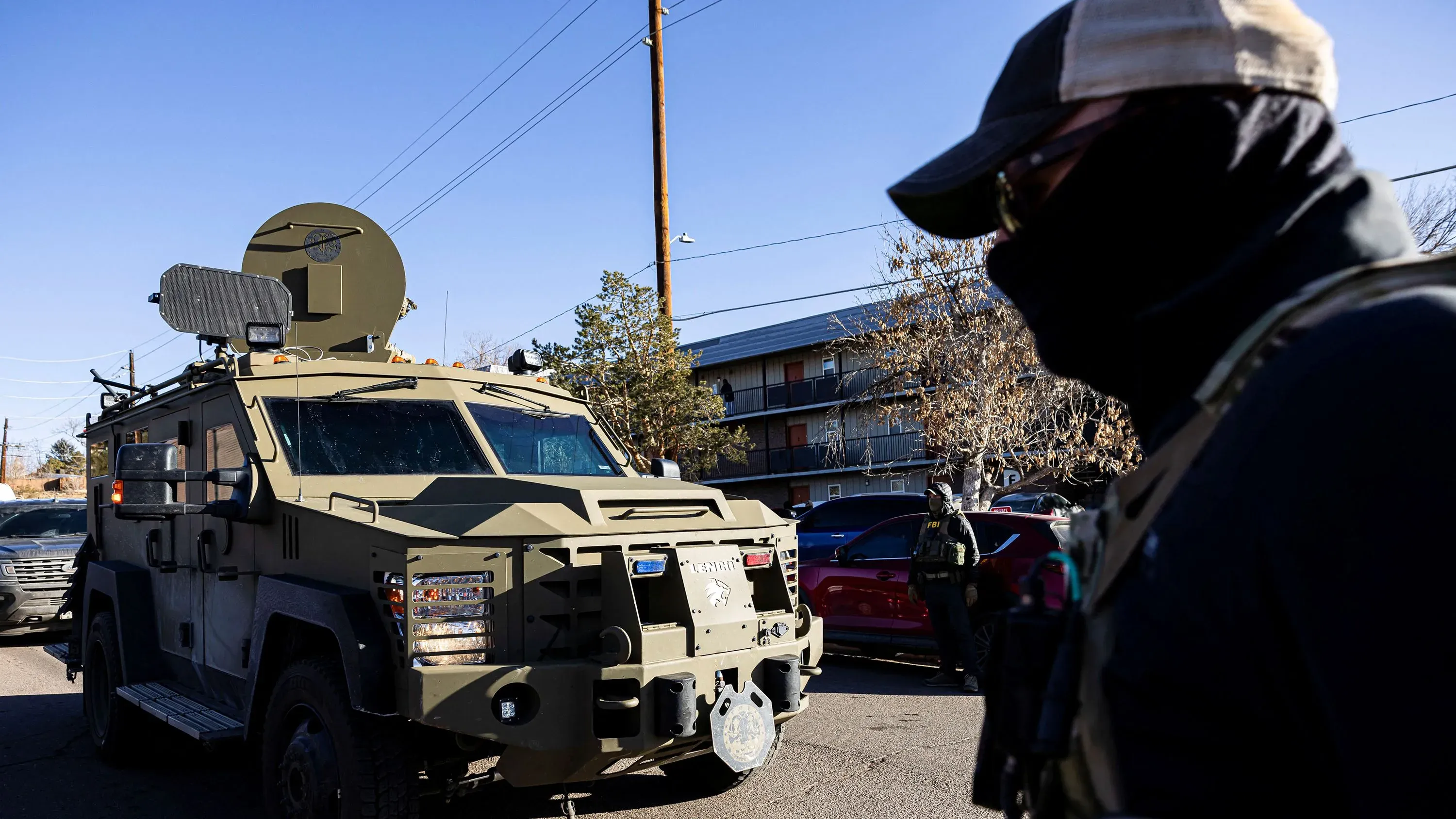 عناصر من إدارة إنفاذ قوانين الهجرة والجمارك يرتدون زيًا عسكريًا بالقرب من مركبة مدرعة، مما يعكس تصعيد الحملة ضد المهاجرين.
