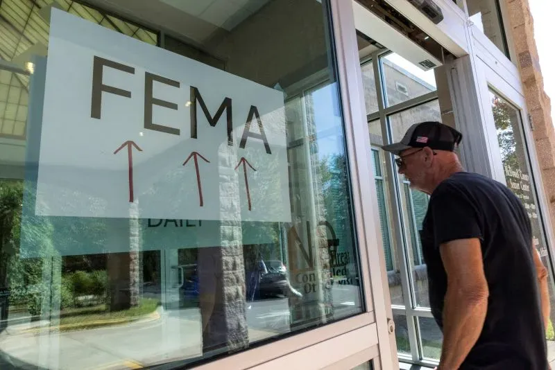 رجل ينظر إلى لافتة تشير إلى وكالة إدارة الطوارئ الفيدرالية (FEMA) على مدخل أحد المكاتب، وسط مخاوف من تخفيضات في الوكالة.