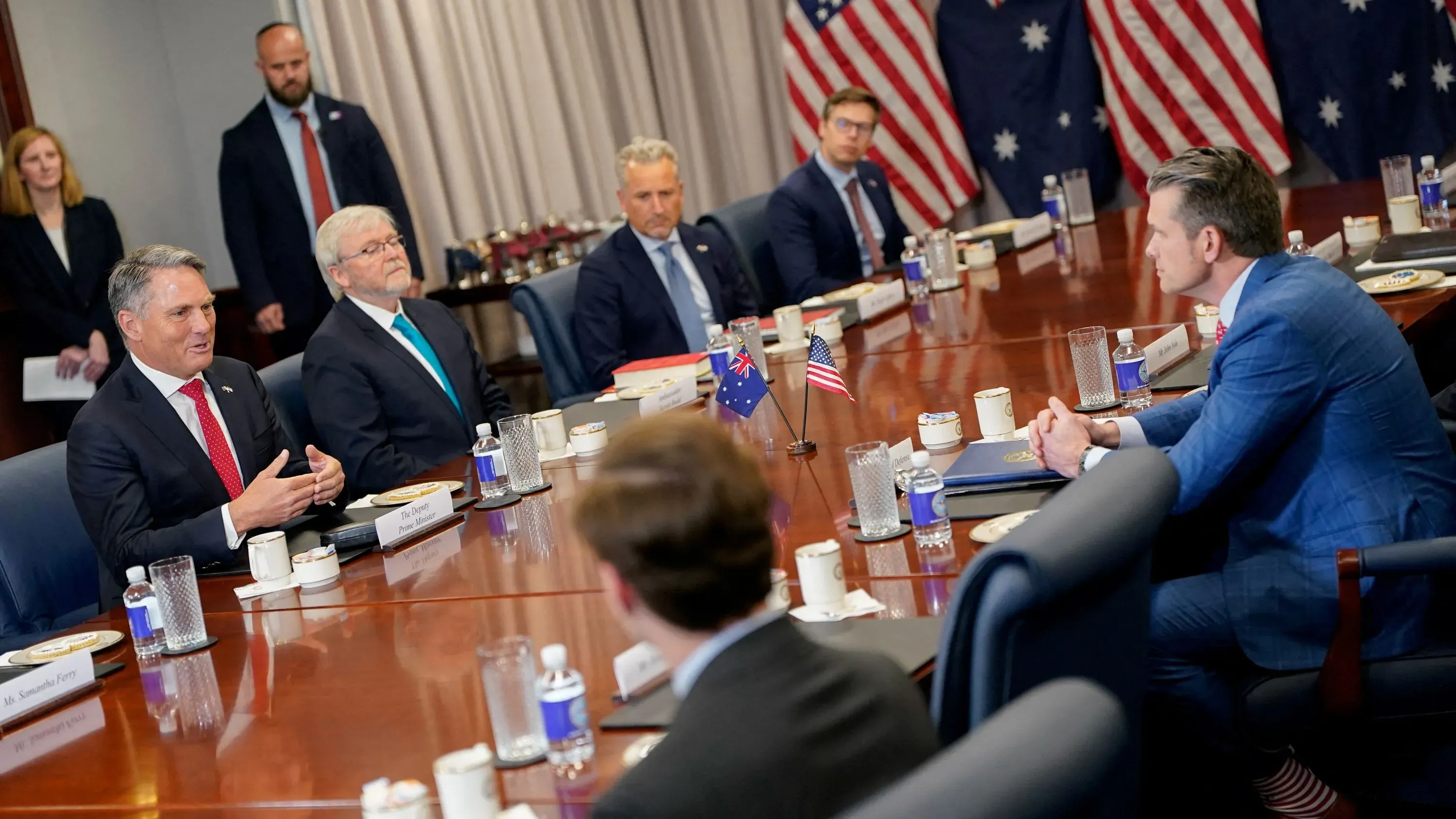 اجتماع لمناقشة اتفاقية "أوكوس" للدفاع، مع وجود مسؤولين أمريكيين وأستراليين، وخلفهم أعلام الولايات المتحدة وأستراليا.