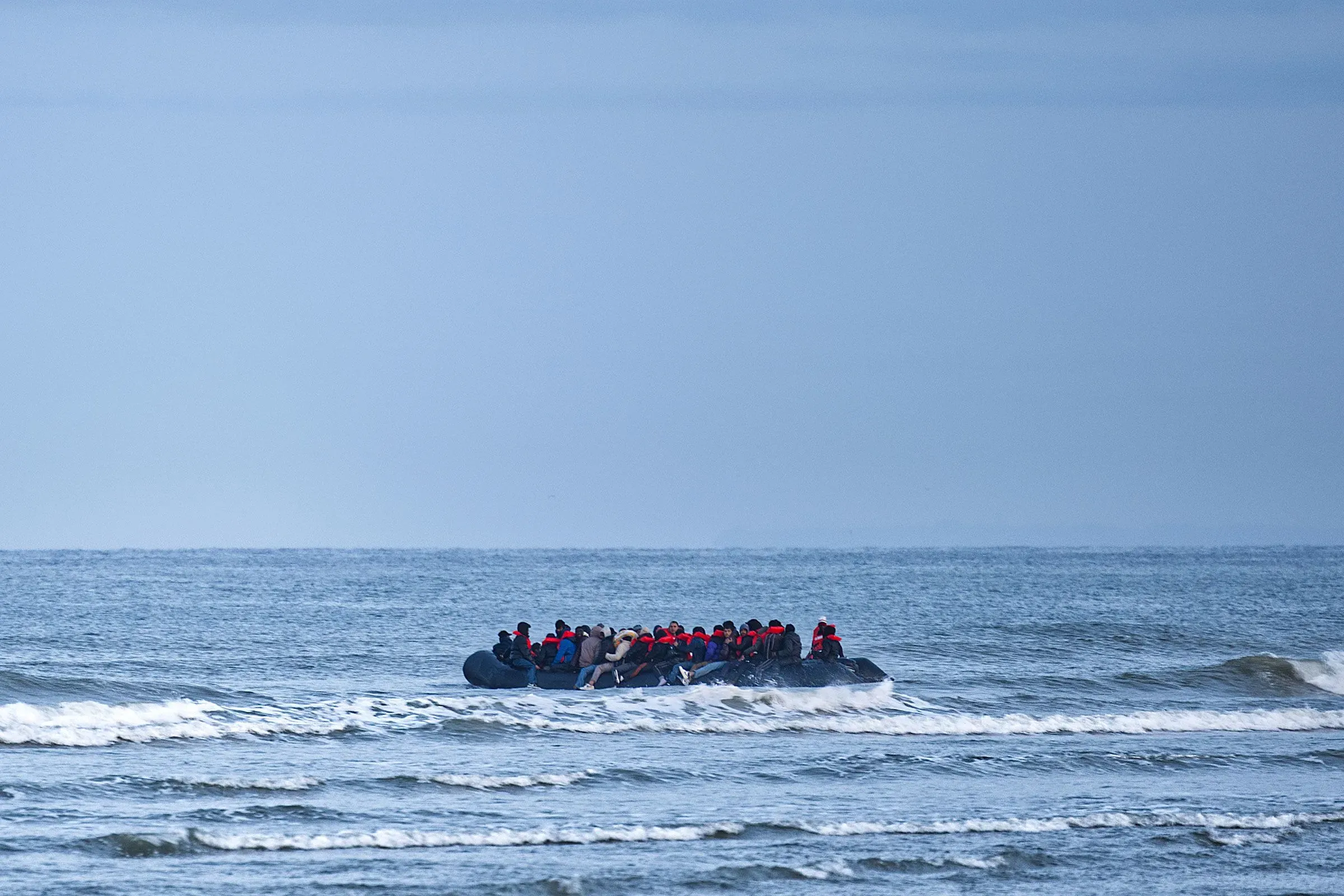 مجموعة من اللاجئين في قارب مطاطي في عرض البحر، تعبير عن تحديات الهجرة واللجوء في ظل السياسات الأمريكية الجديدة.