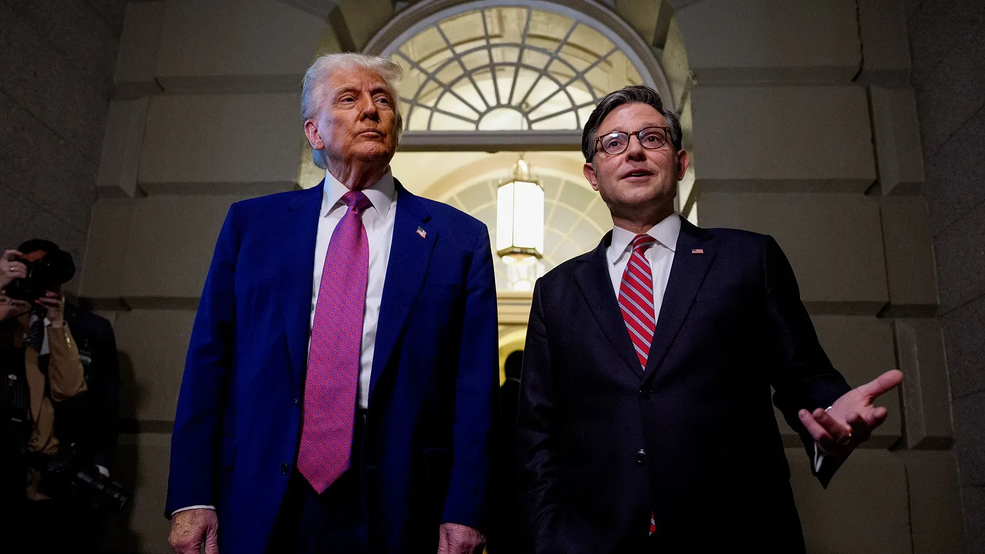 الرئيس دونالد ترامب يقف مع مستشار في مبنى الكونغرس، مع التركيز على التوترات الاقتصادية وتأثير مشروع قانون الضرائب على الأسواق المالية.