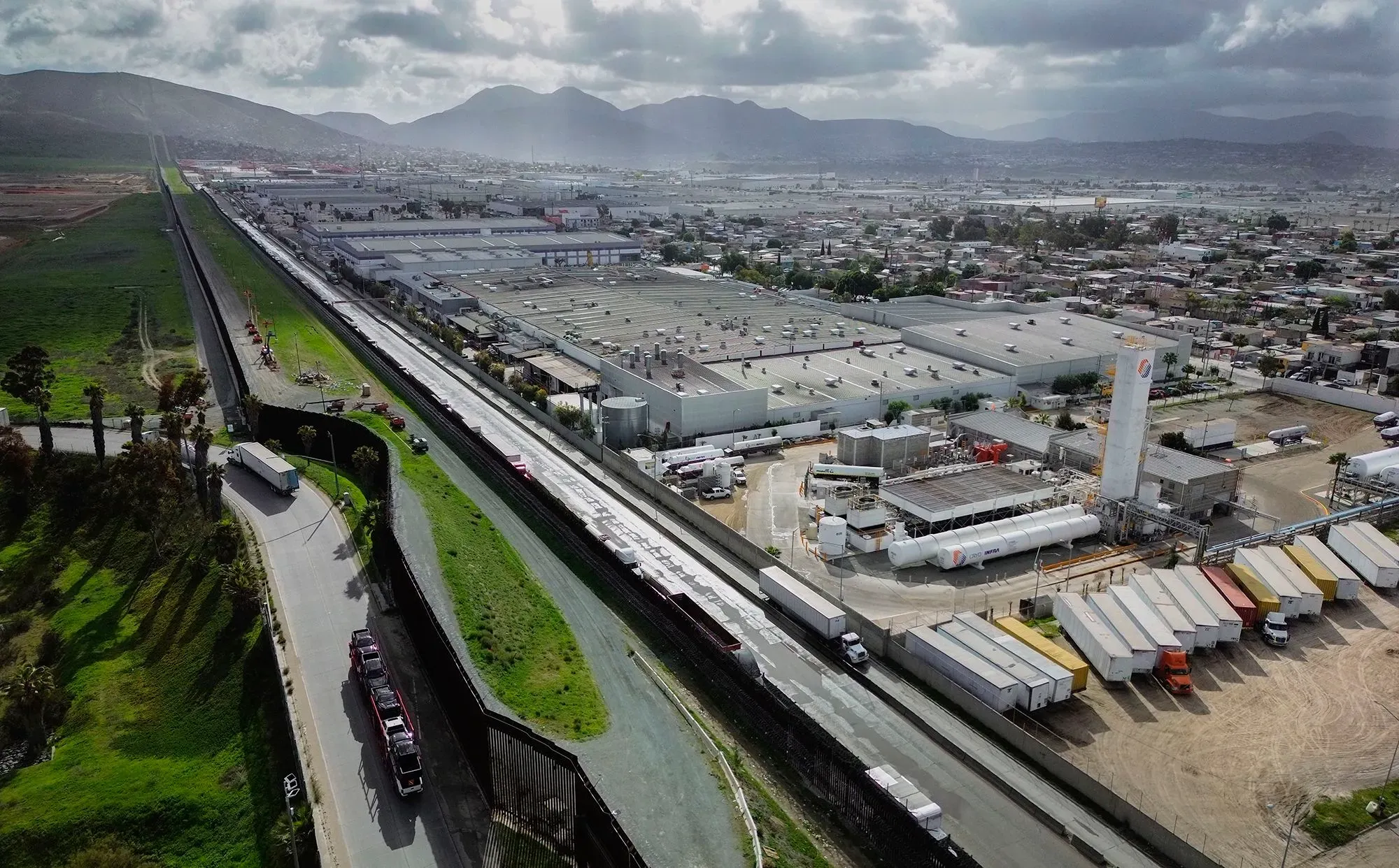 صورة تظهر الحدود بين الولايات المتحدة والمكسيك، مع شاحنات تجارية تنتظر العبور، تعكس العلاقات التجارية المتوترة بين البلدين.