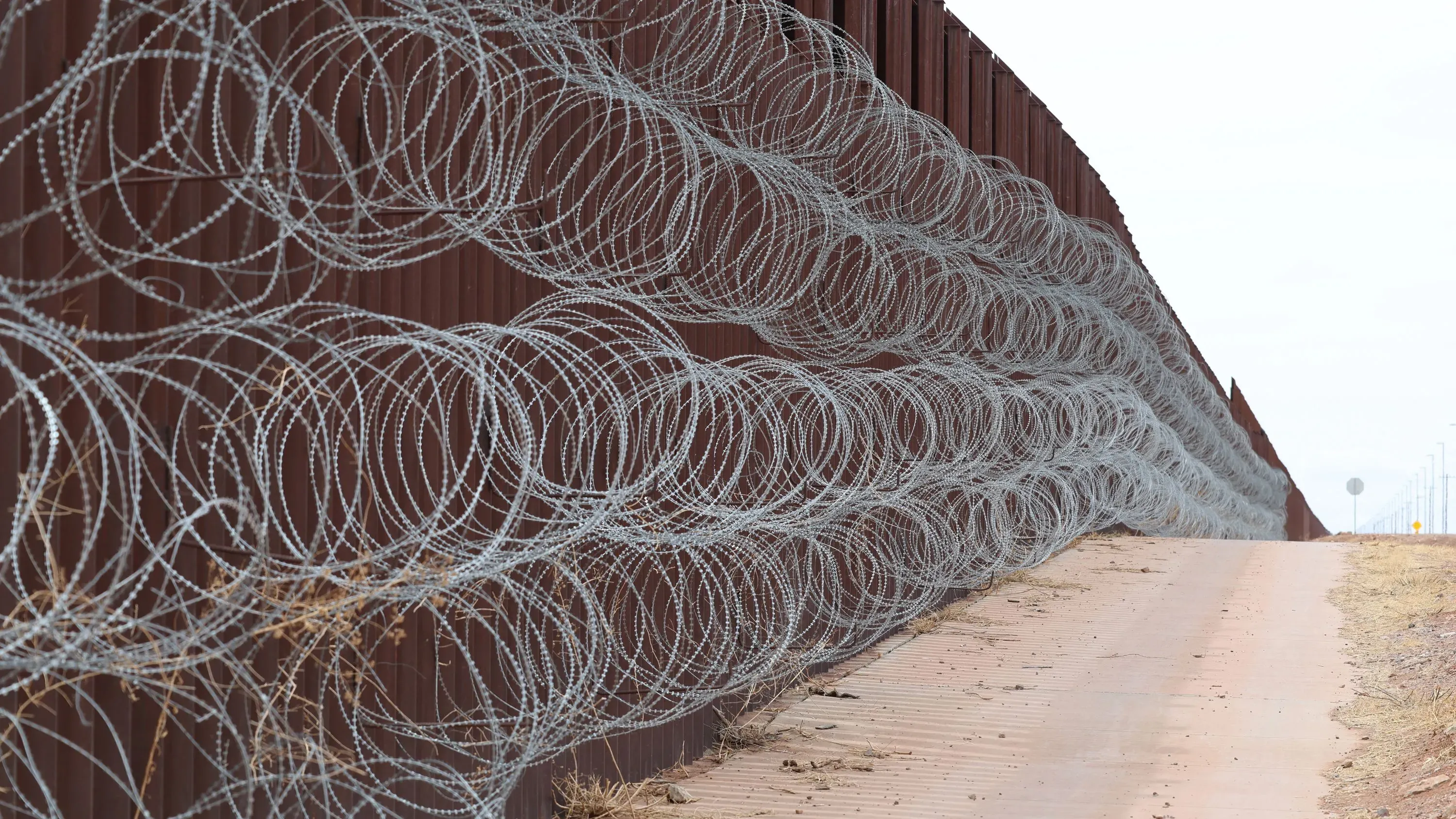 سياج حدودي محاط بسياج شائك على طول الحدود الأمريكية المكسيكية، يعكس جهود تأمين الحدود وتعزيز السيطرة العسكرية.