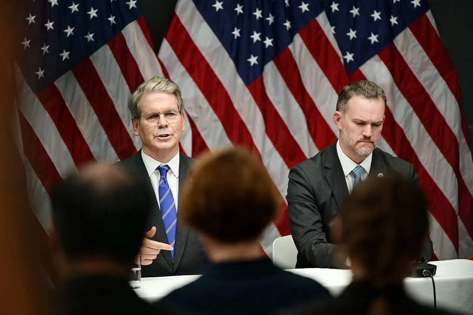 اجتماع لمفاوضي ترامب مع مسؤولين أمريكيين، مع العلم الأمريكي خلفهم، يناقش قضايا التجارة مع الصين.