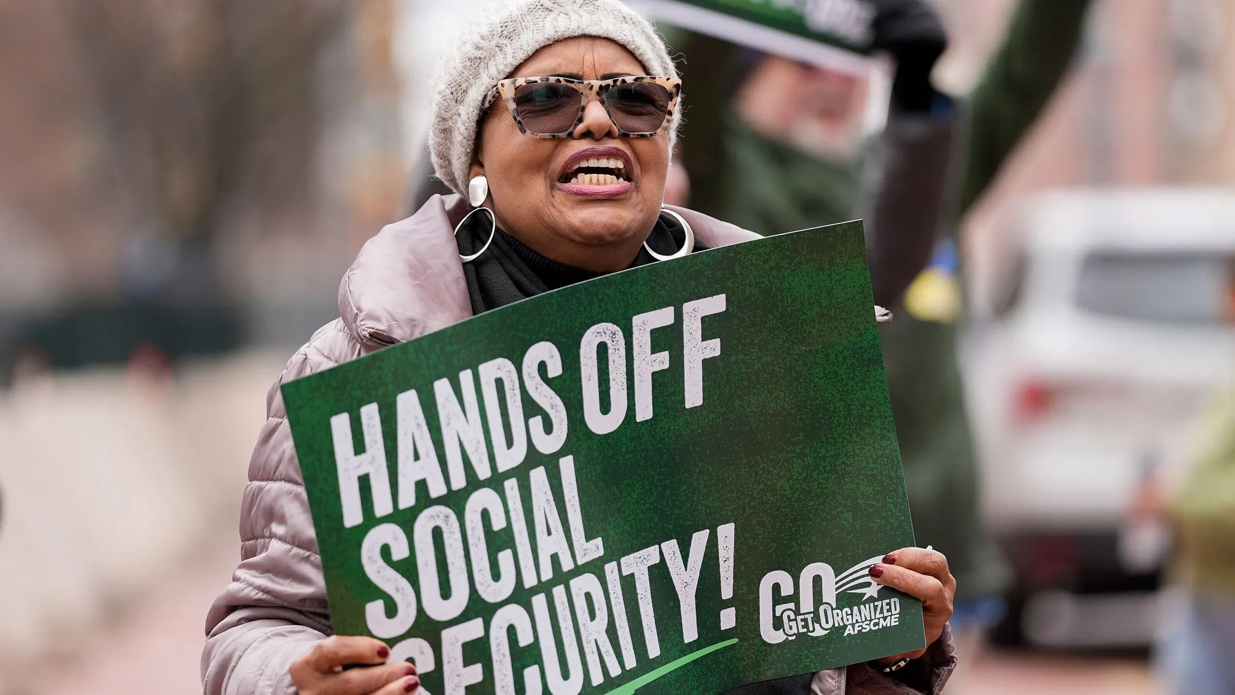 امرأة تحمل لافتة مكتوب عليها "أبعدوا أيدكم عن الضمان الاجتماعي" أثناء احتجاج، تعبيراً عن القلق بشأن الوصول إلى بيانات الضمان الاجتماعي.
