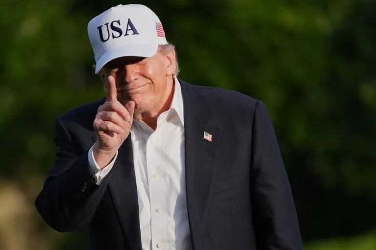 ترامب مبتسم ويرتدي قبعة مكتوب عليها "USA"، يشير بإصبعه إلى الأعلى، مما يعكس موقفه الإيجابي تجاه المفاوضات مع إيران.
