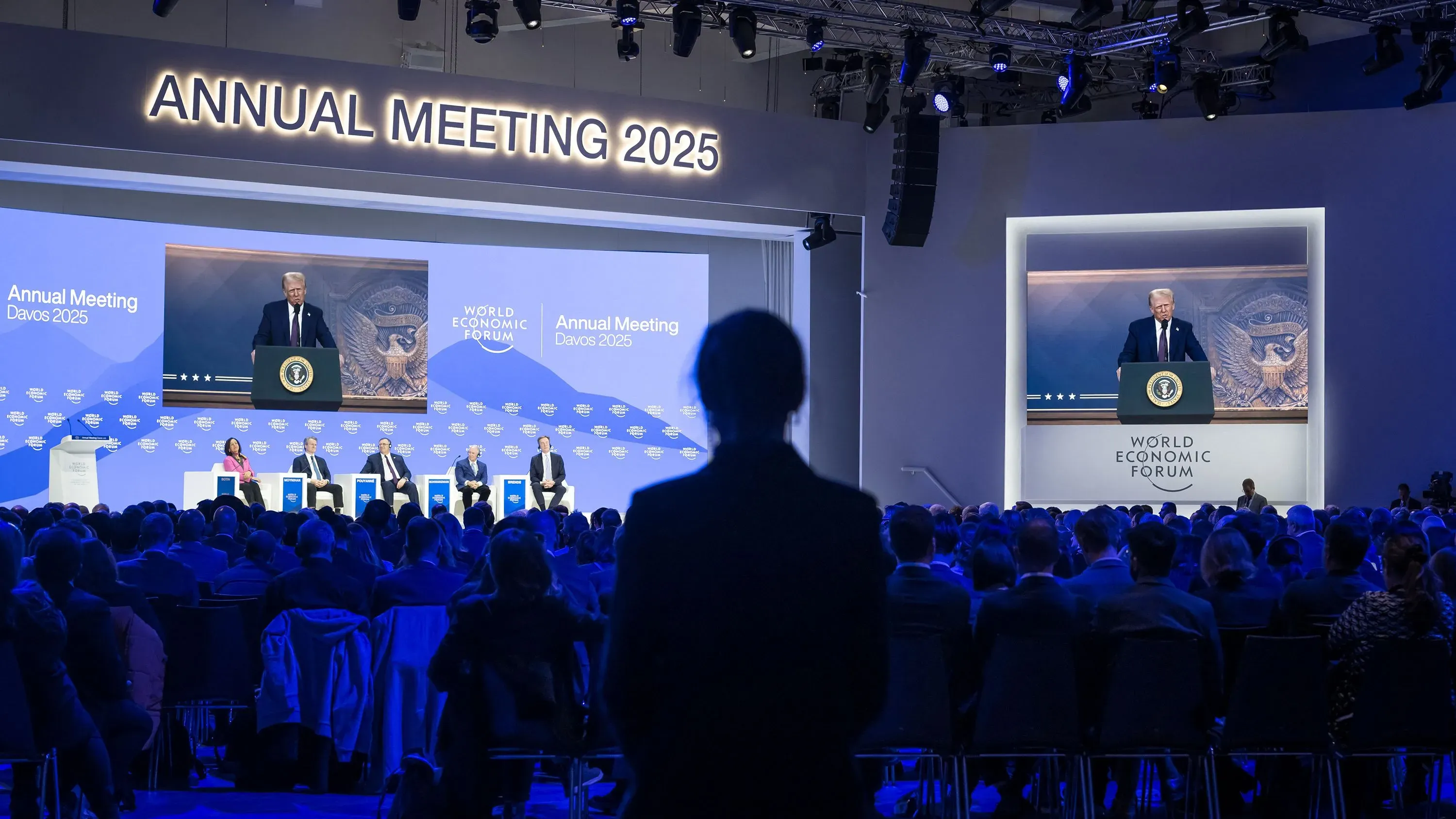 خطاب ترامب في المنتدى الاقتصادي العالمي بدافوس، مع التركيز على خطته الاقتصادية الجديدة، وخلفيته تضم جمهورًا كبيرًا.