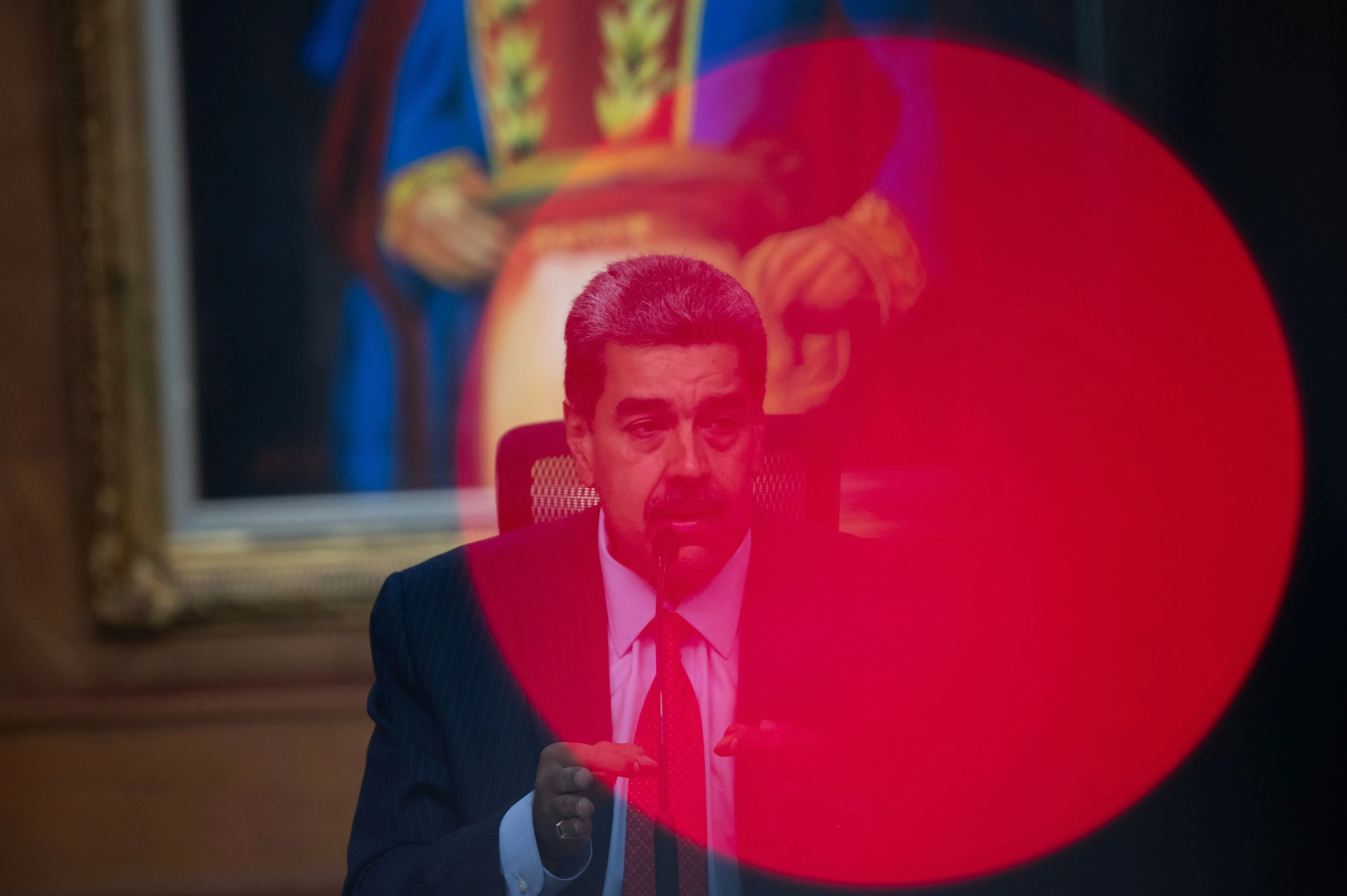 نيكولاس مادورو، الرئيس الفنزويلي، يتحدث خلال مؤتمر صحفي، مع وجود صورة خلفية له. المكافأة المقدمة للقبض عليه تعكس تهم تهريب المخدرات.
