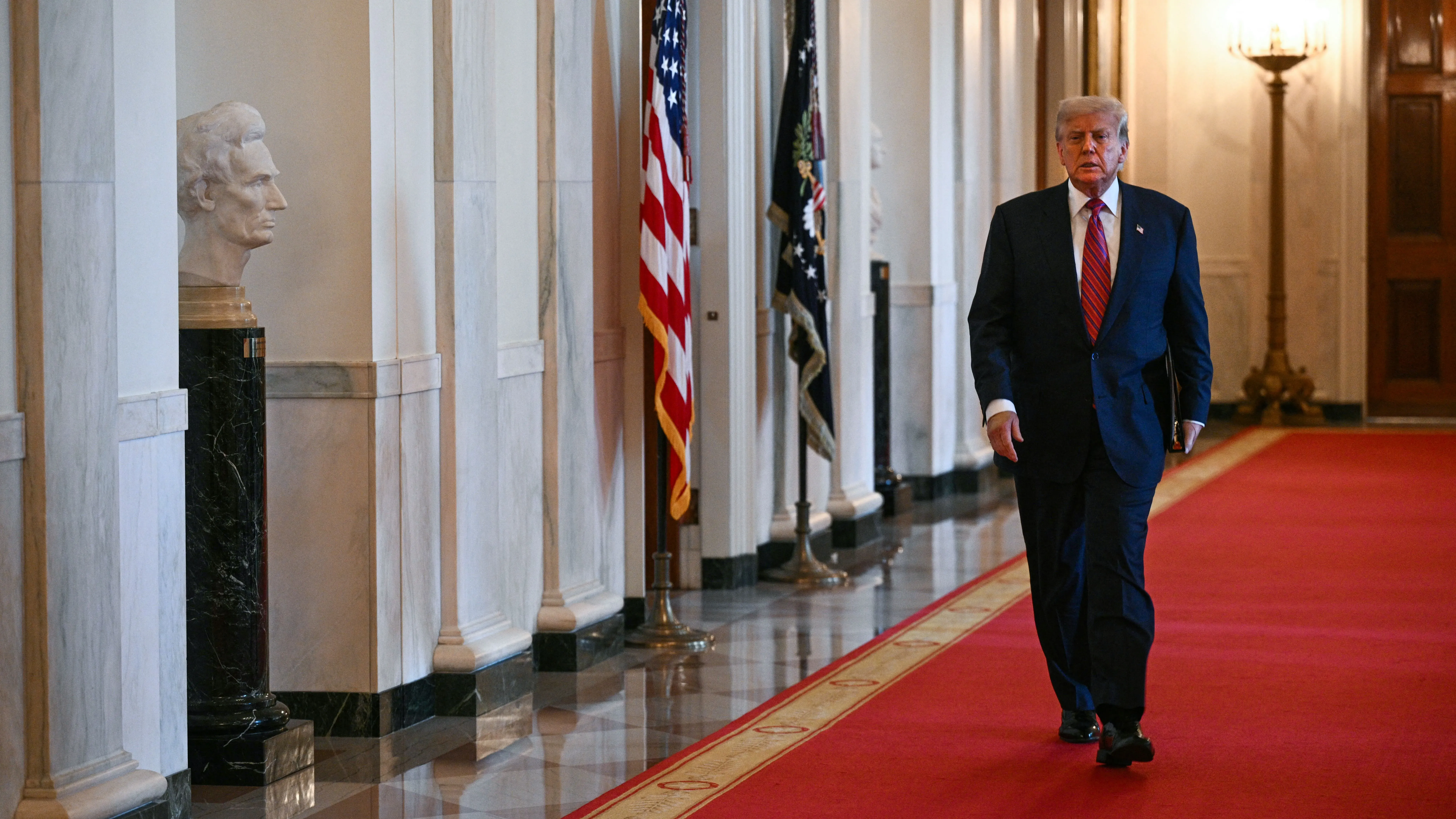 ترامب يسير في ممر مزين بالعلم الأمريكي، بينما يظهر تمثال نصفي لأبراهام لينكولن على اليسار، في سياق دعوى التشهير ضد صحيفة وول ستريت جورنال.