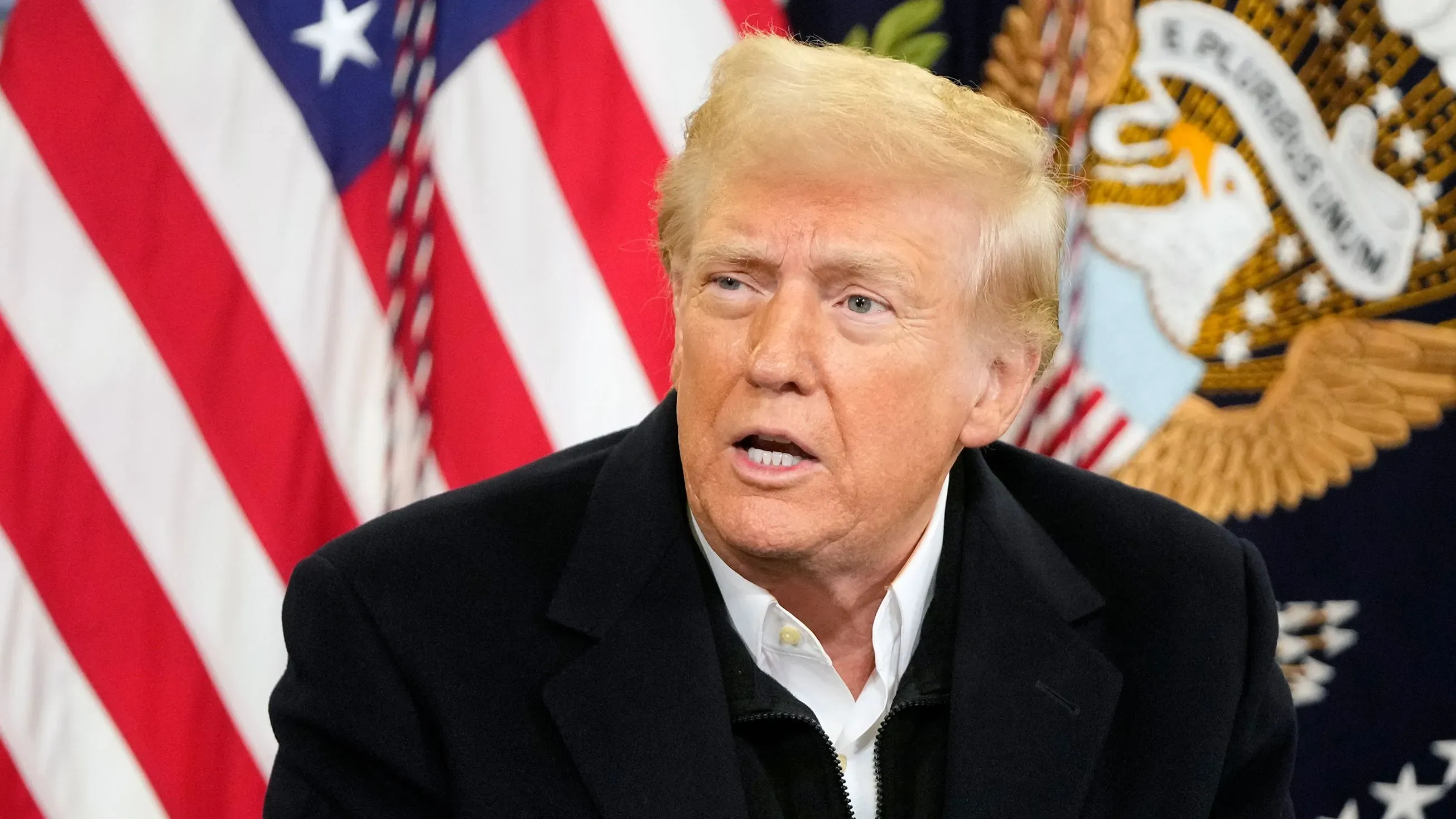 تظهر الصورة الرئيس دونالد ترامب أثناء حديثه خلف علم الولايات المتحدة وشعار الرئاسة، محاطًا بأجواء رسمية.
