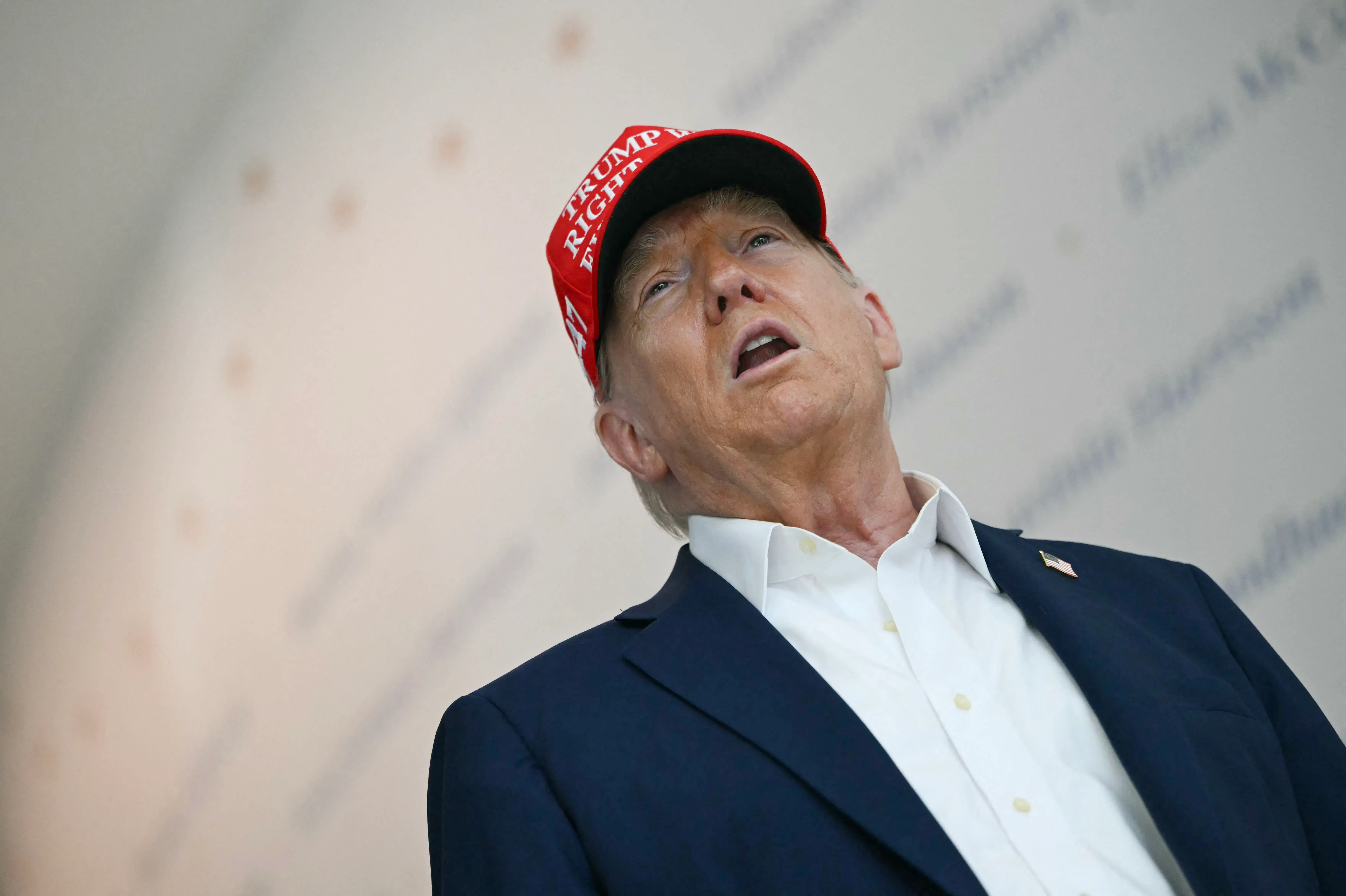 ترامب يتحدث في مناسبة عامة، مرتديًا قبعة تحمل شعار حملته. تعكس تعابير وجهه قلقًا حول قضايا اقتصادية.