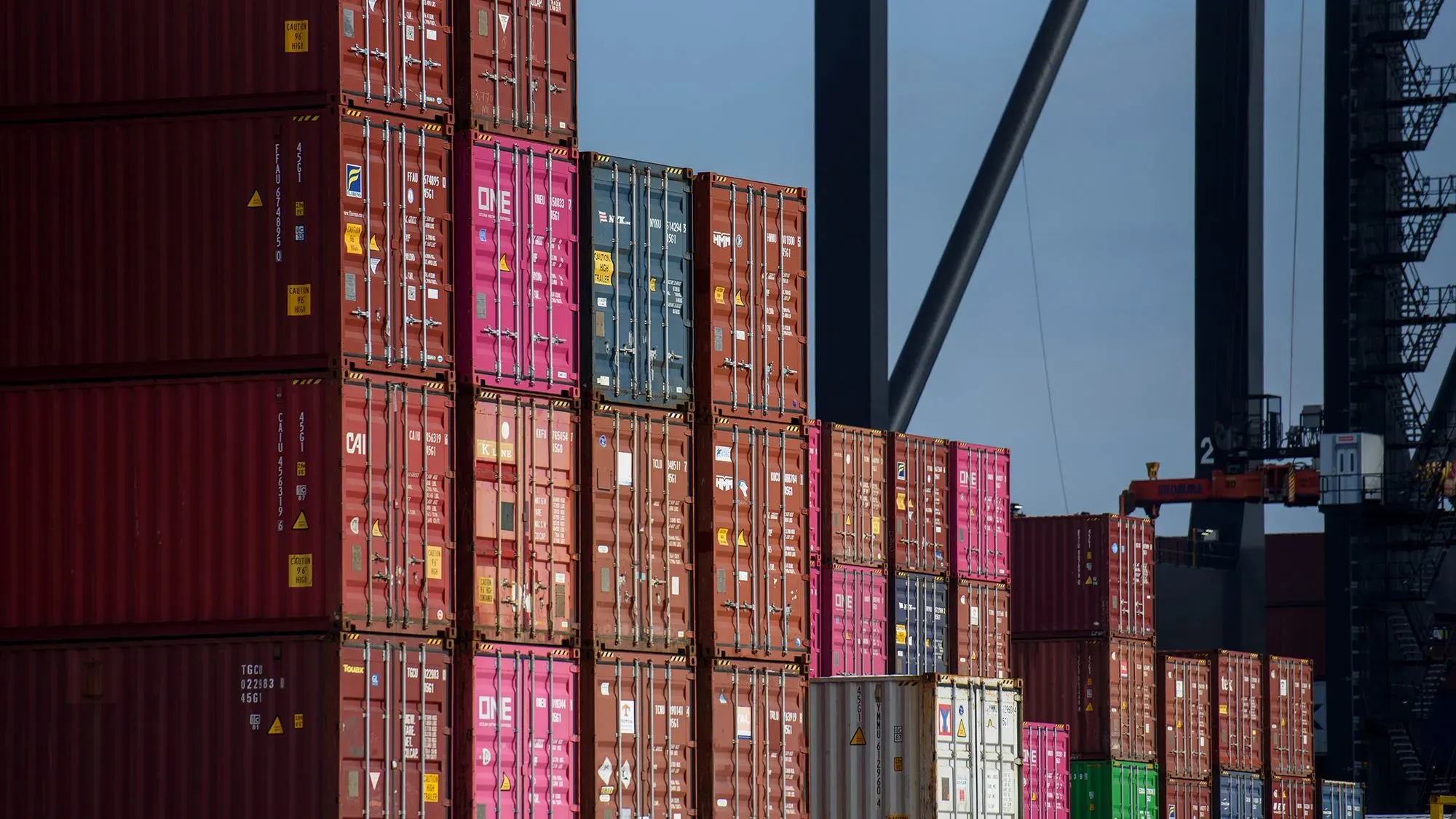 حاويات شحن ملونة مكدسة في ميناء، تشير إلى تأثير التعريفات الجمركية على التجارة العالمية والاقتصاد الأمريكي.