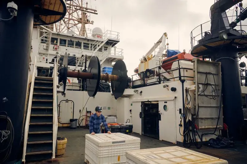 صورة تظهر عالماً يعمل على متن سفينة أبحاث بحرية، حيث تُستخدم المعدات لجمع بيانات حول المحيطات.