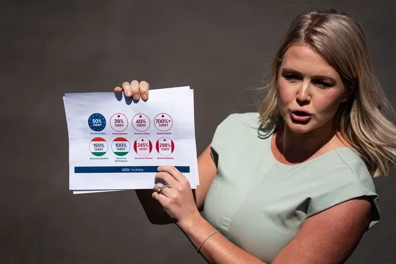 امرأة تعرض ورقة تحتوي على معلومات حول تعريفات جمركية مختلفة، مع التركيز على الأرقام والنسب المئوية.