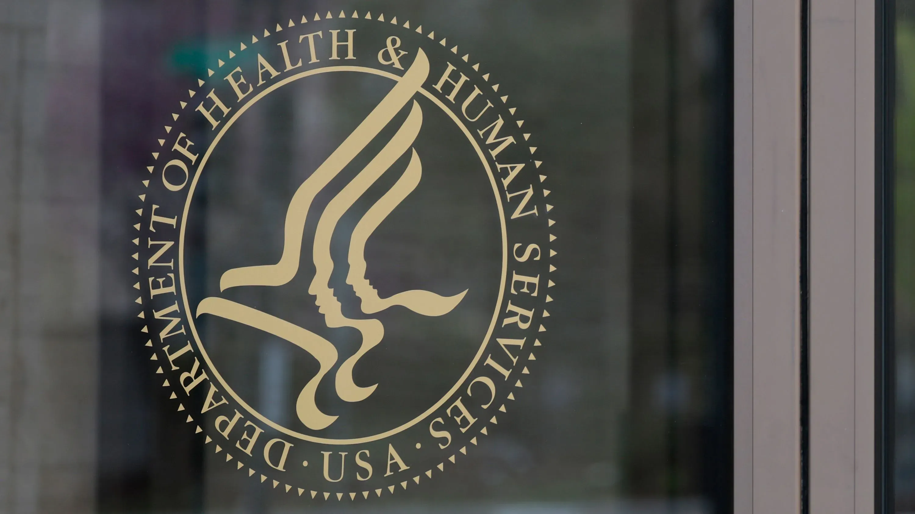 شعار وزارة الصحة والخدمات الإنسانية الأمريكية، يظهر تصميمه الذهبي على نافذة زجاجية، مع التركيز على خدمات الصحة والرعاية الاجتماعية.