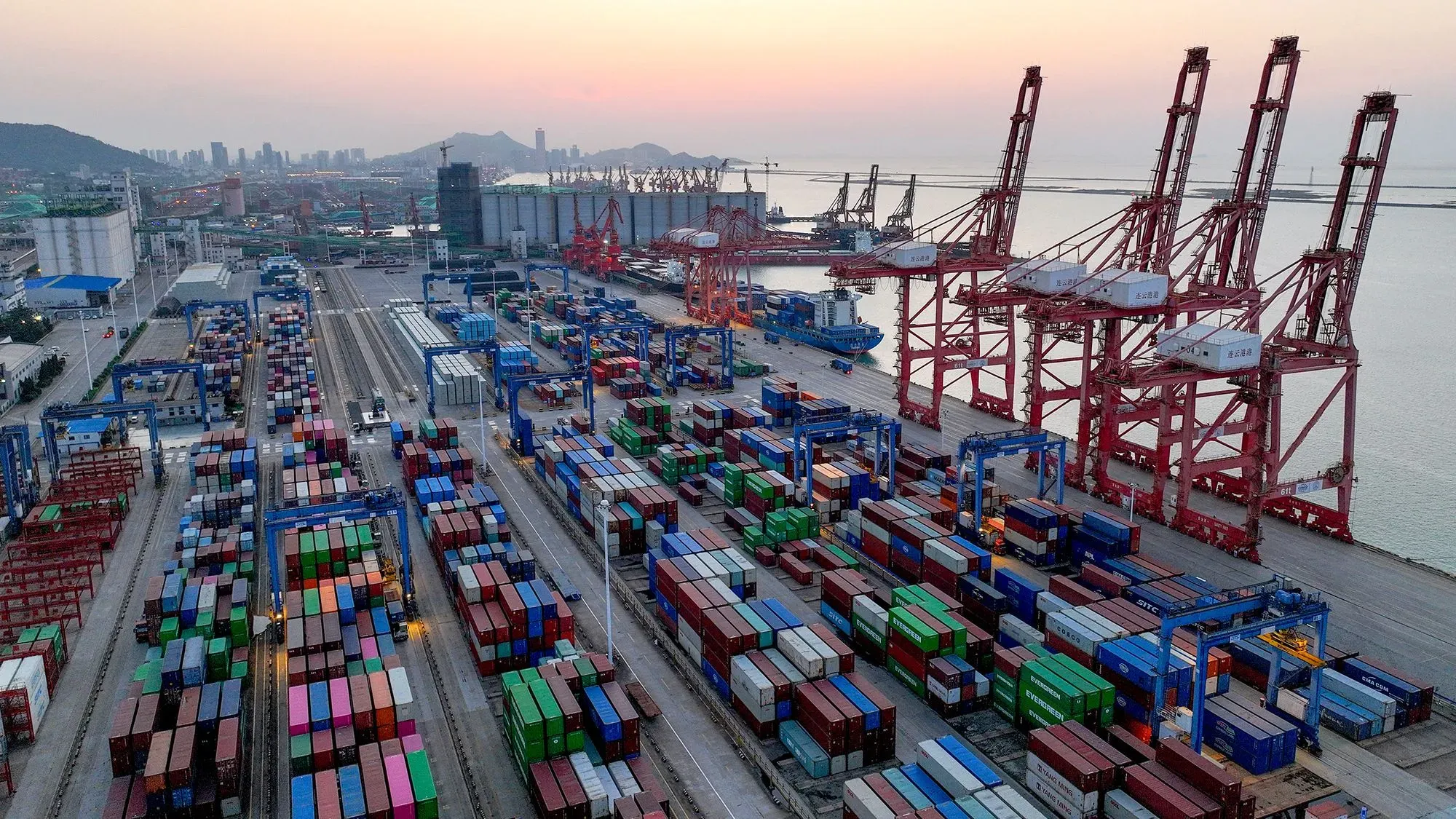 صورة لميناء يحتوي على حاويات شحن ملونة وأوناش تحميل، تعكس تأثير الحرب التجارية بين الولايات المتحدة والصين.