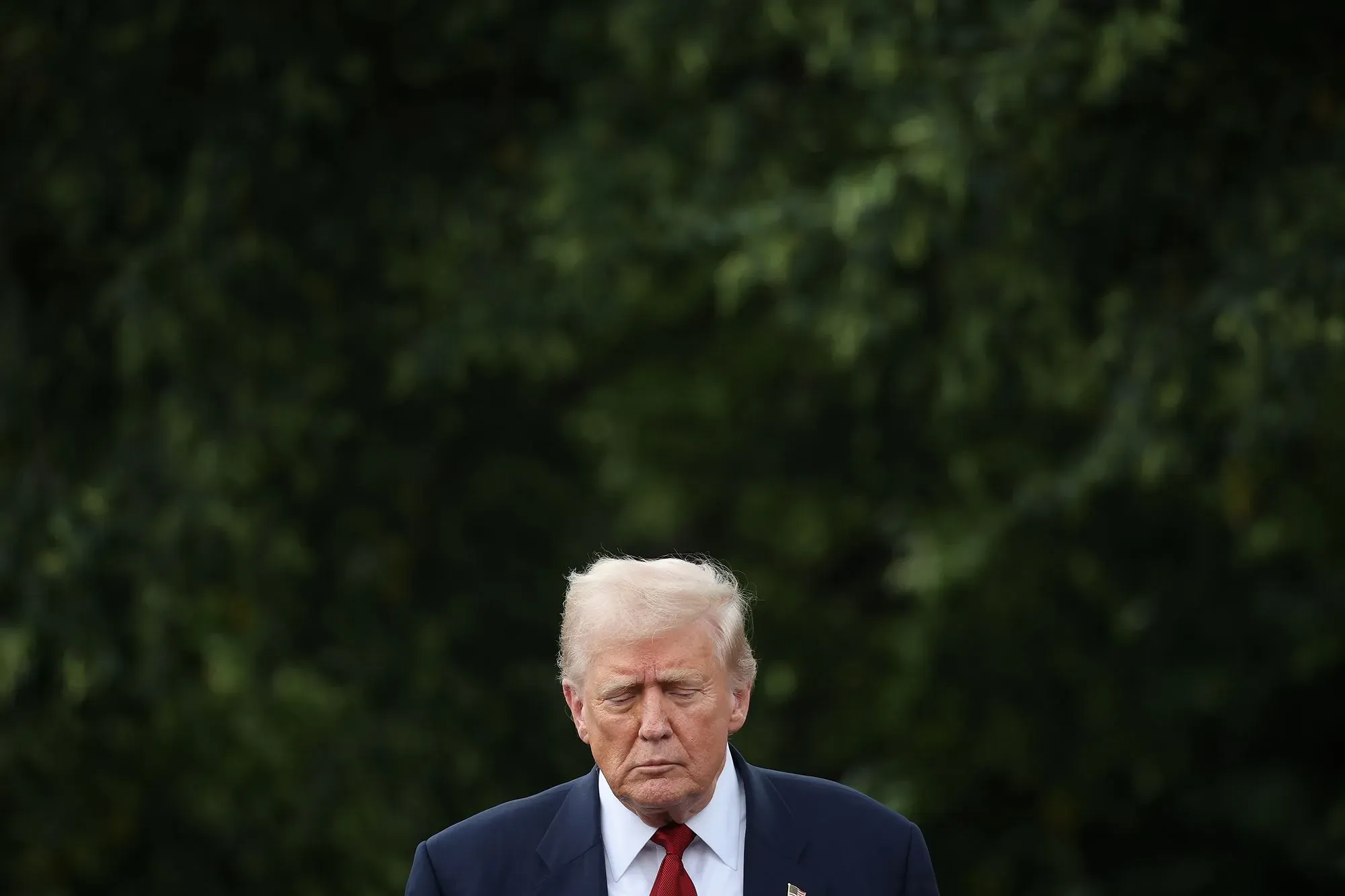 دونالد ترامب يتحدث بجدية أثناء إعلان تعيينات اقتصادية مهمة، وسط خلفية خضراء، مما يعكس التوترات حول الاقتصاد الأمريكي.