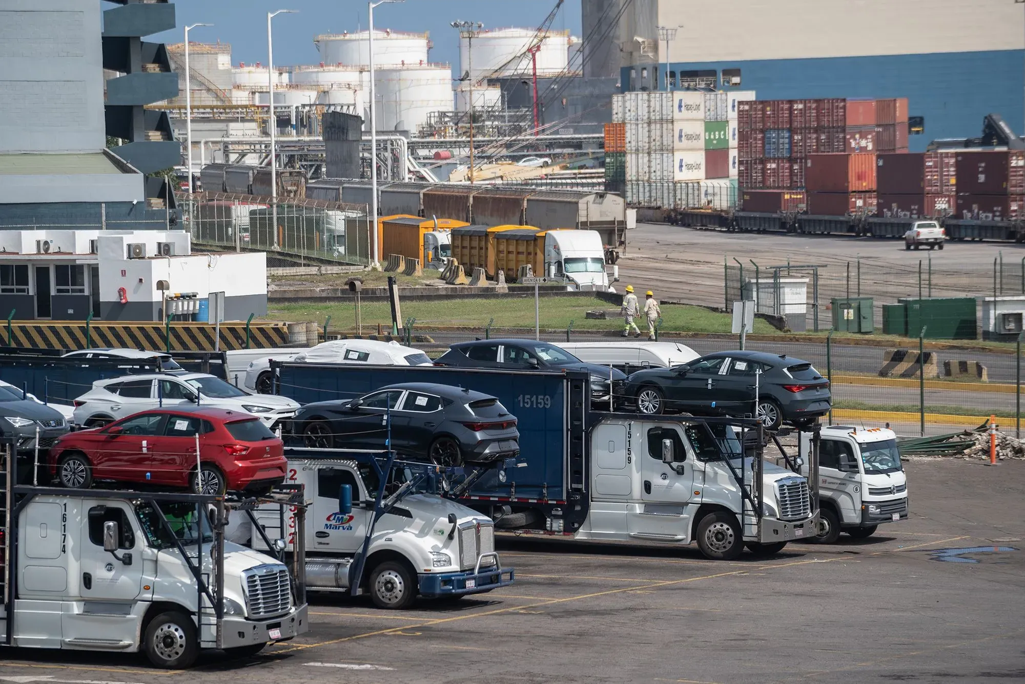 شاحنات نقل تحمل سيارات في ميناء، مع حاويات شحن في الخلفية، تعكس تأثير اتفاقية USMCA على التجارة بين الولايات المتحدة وكندا والمكسيك.