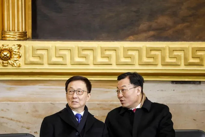 اجتماع لمستشارين صينيين يتبادلون الحديث في إطار التوترات التجارية مع الولايات المتحدة، مع خلفية مزخرفة تشير إلى الأهمية السياسية.