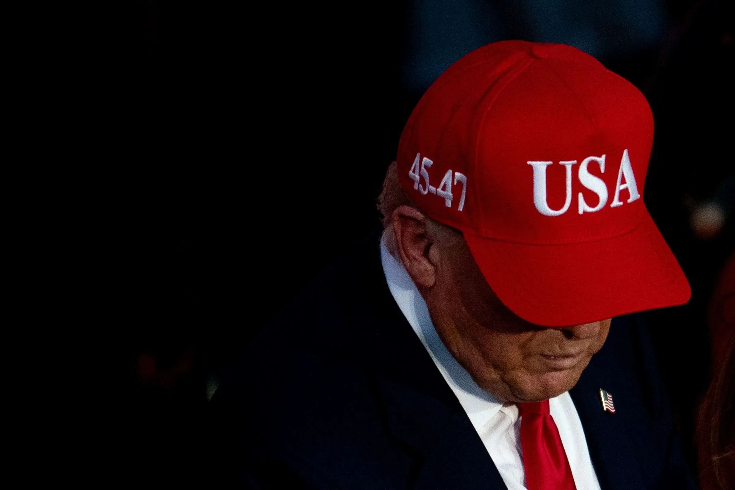 ترامب يرتدي قبعة حمراء مكتوب عليها "USA" بينما ينظر إلى الأسفل، في سياق حديثه عن إنهاء الإغلاق الحكومي.