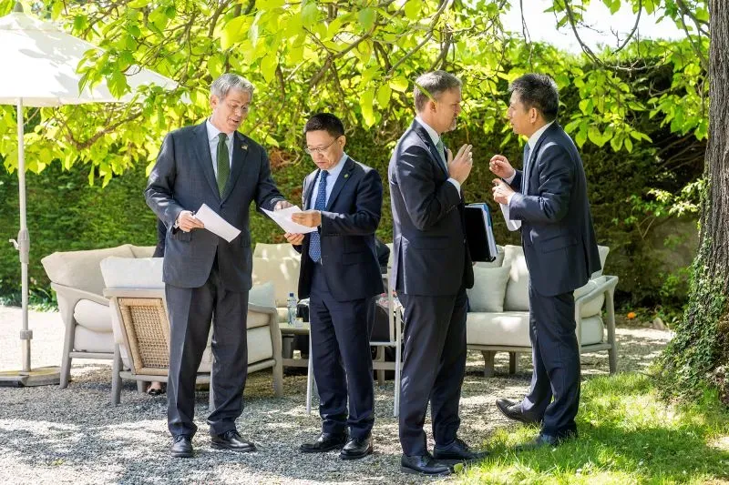 اجتماع مسؤولين حكوميين أمريكيين وصينيين في حديقة، حيث يناقشون تخفيض الرسوم الجمركية على البضائع الصينية.