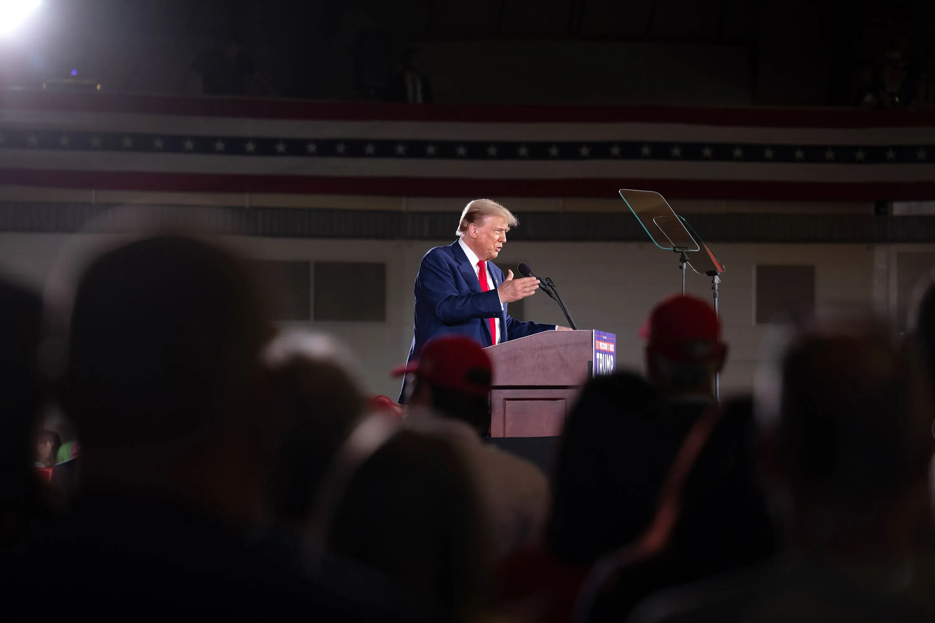 ترامب يتحدث في تجمع انتخابي، محاط بجمهور يرتدي قبعات حمراء، مع العلم الأمريكي في الخلفية، مما يعكس تراجع دعمه بين اللاتينيين.