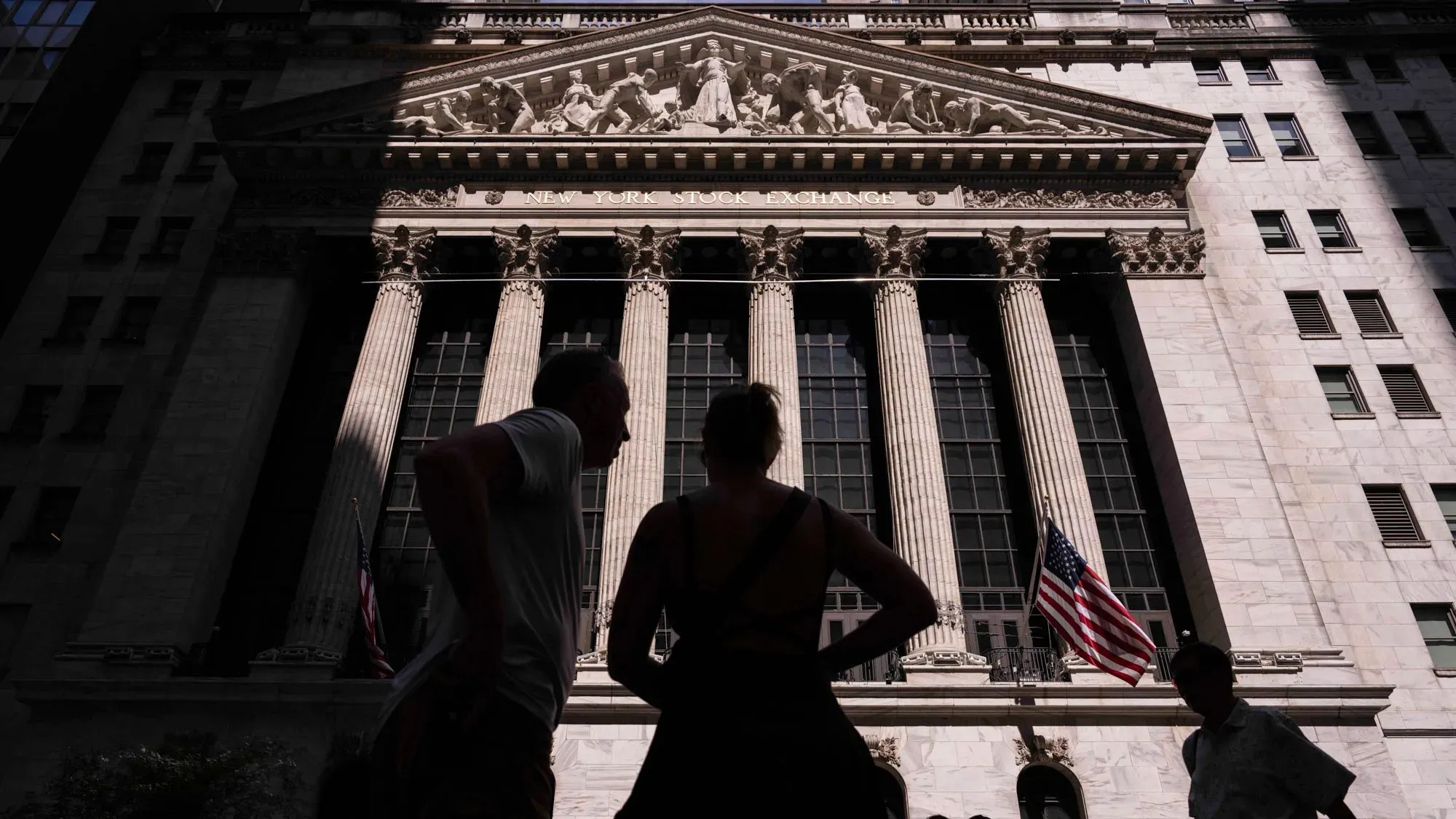 واجهة بورصة نيويورك، مع أشخاص يقفون في الظل، تعكس قلق المستثمرين حول استقلالية الاحتياطي الفيدرالي في ظل تصريحات ترامب.