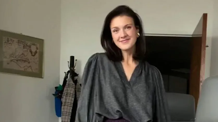 موظفة في مكتب إدارة شؤون الموظفين ترتدي ملابس أنيقة وتبتسم للكاميرا، مع تفاصيل عن نشاطها كمؤثرة في الموضة على إنستغرام.