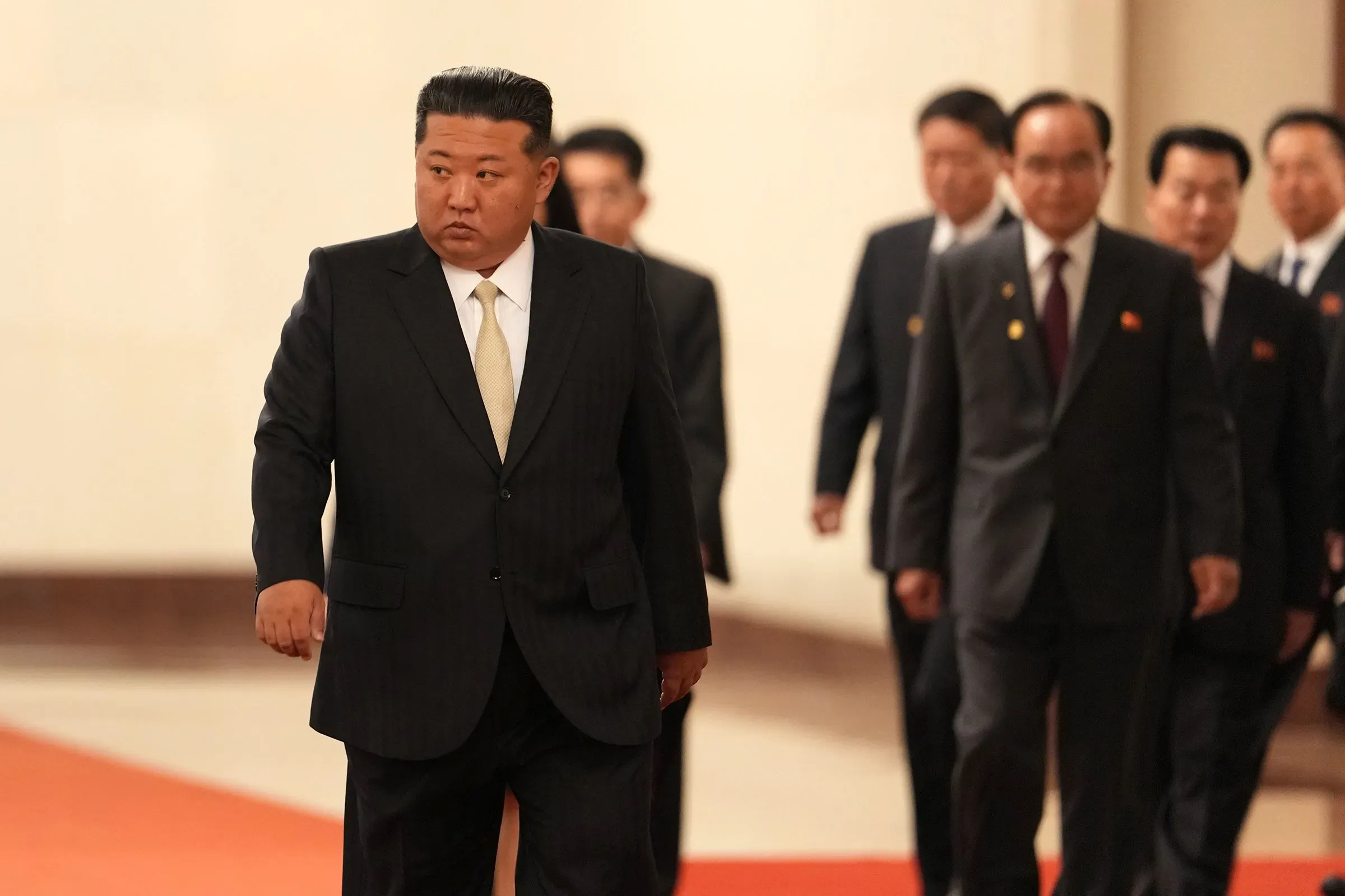 كيم جونغ أون يسير برفقة مسؤولين آخرين في حدث رسمي، مع التركيز على تعبيرات وجهه وملابسه الرسمية، مما يعكس أهمية اللقاءات السياسية.