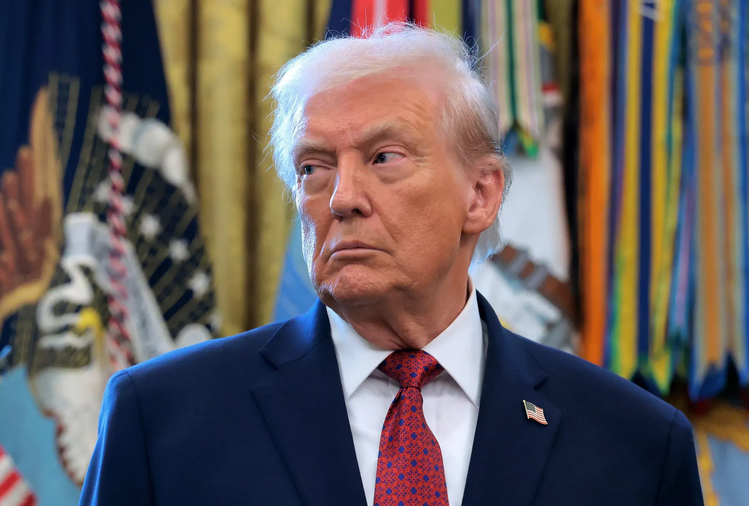 ترامب يتحدث في المكتب البيضاوي، مع خلفية تتضمن الأعلام العسكرية، مشيرًا إلى فرض حصار على النفط الفنزويلي.