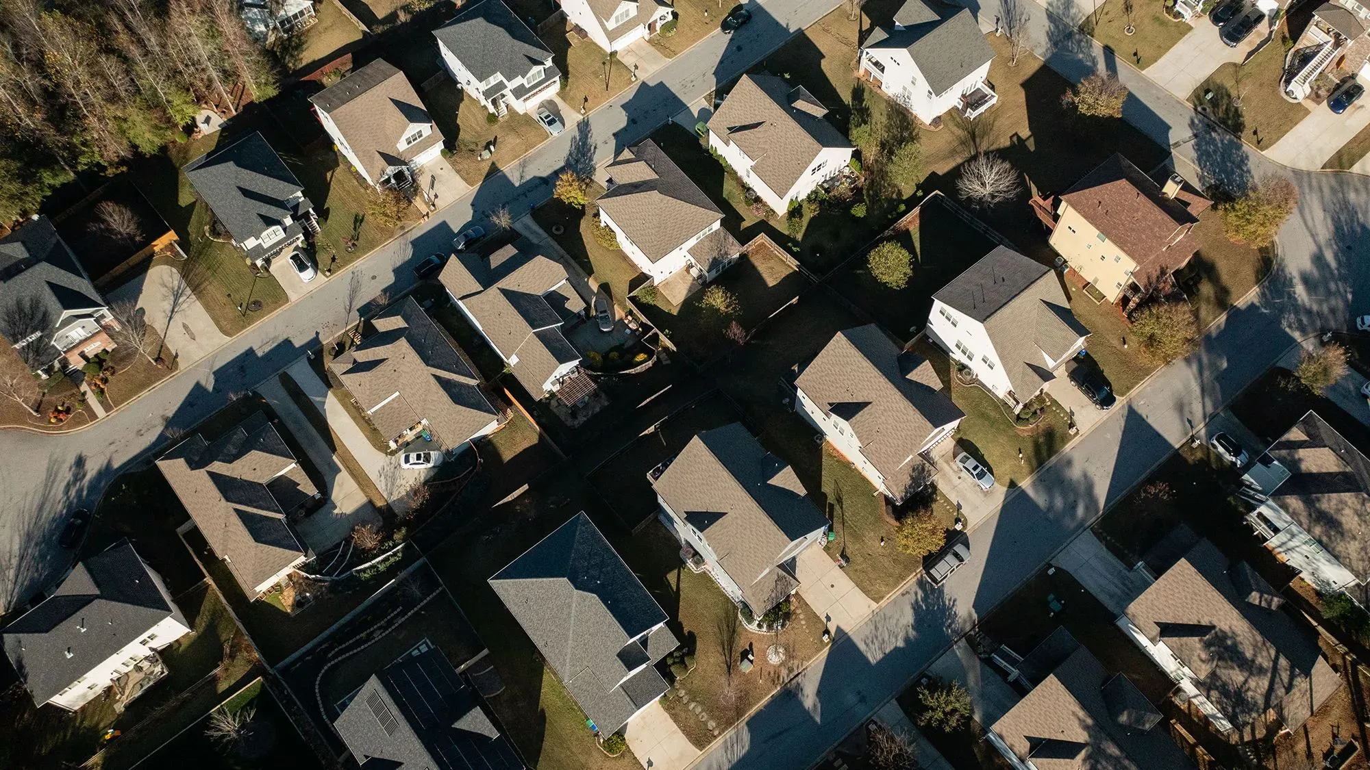 لقطة جوية لحي سكني يظهر منازل ذات أسطح مائلة وشوارع متعرجة، تعكس تحديات الإسكان العادل وتنوع المجتمعات.