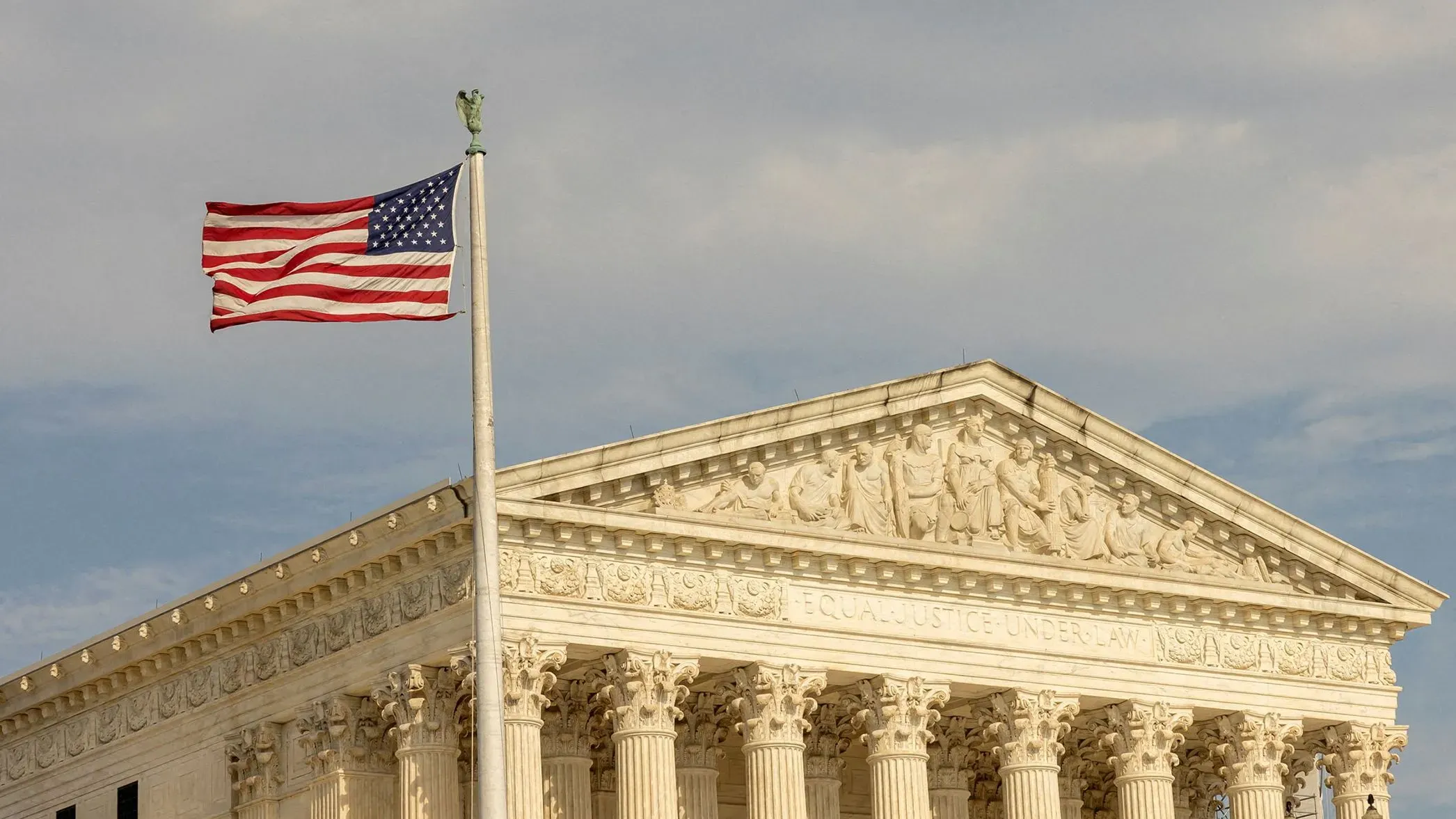 مبنى المحكمة العليا الأمريكية مع العلم الأمريكي يرفرف في المقدمة، مما يرمز إلى القضايا القانونية المتعلقة بسلطة الرئيس ترامب.