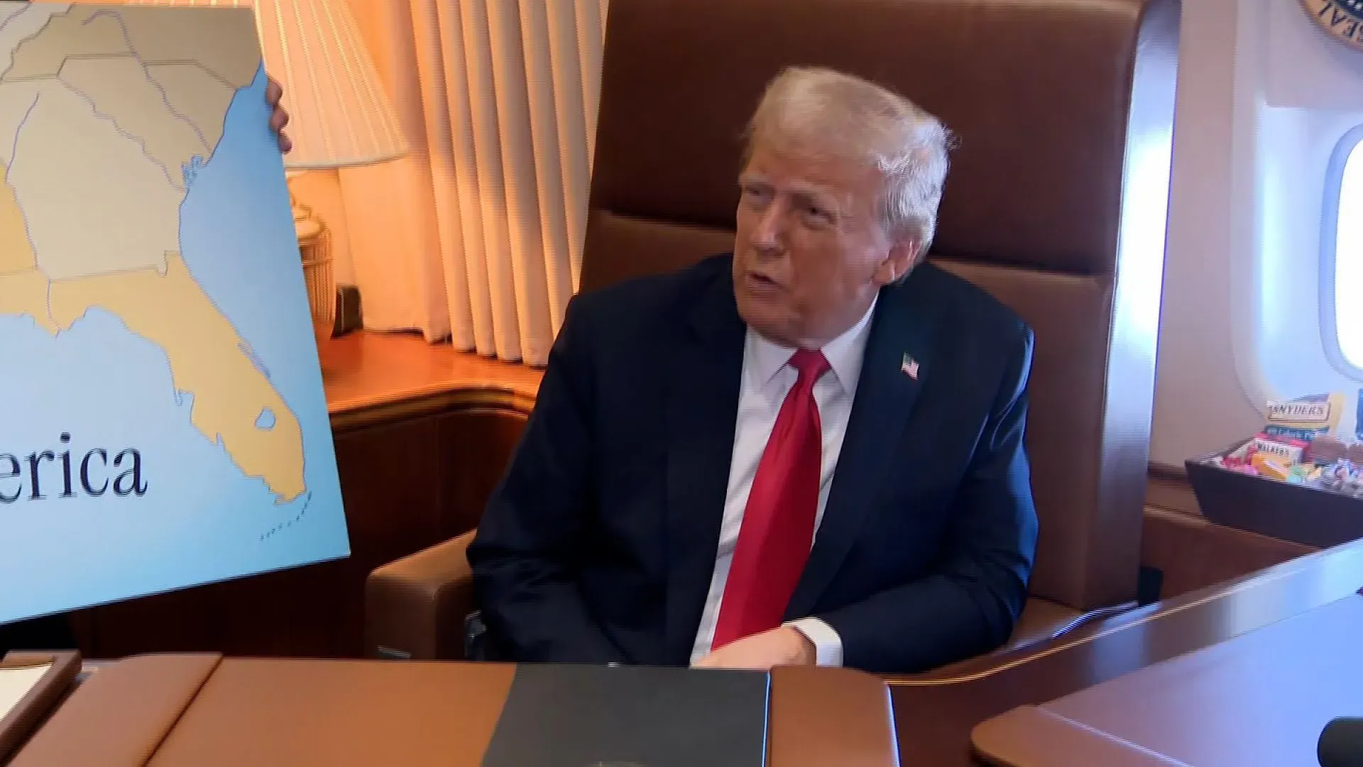 دونالد ترامب يتحدث للصحفيين على متن طائرة الرئاسة، ممسكًا بخريطة، معلنًا عن خطط لفرض رسوم جمركية على واردات الصلب والألومنيوم.