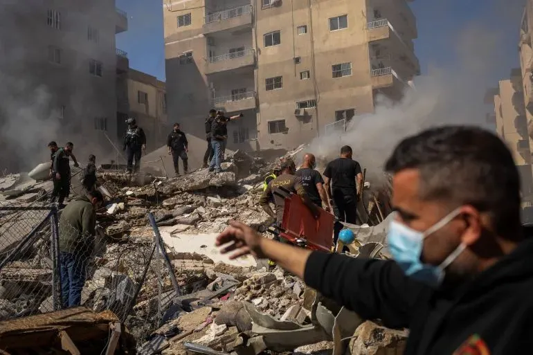 دخان يتصاعد من مبانٍ مدمرة في لبنان، حيث يتجمع رجال الإنقاذ وسط الأنقاض بعد هجوم إسرائيلي، مما يزيد من معاناة السكان.