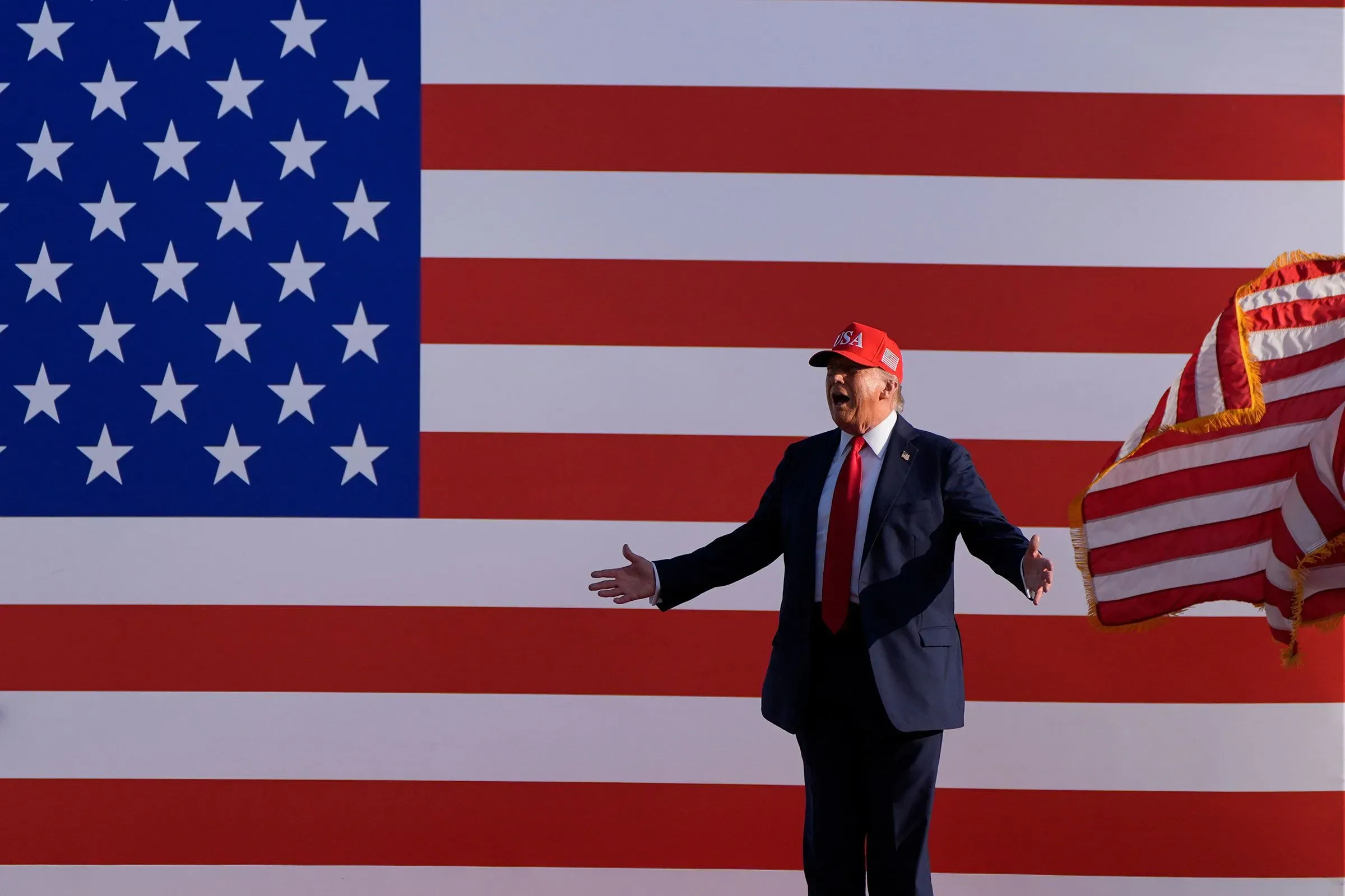 دونالد ترامب يقف أمام علم الولايات المتحدة، معبرًا عن آرائه حول الديكتاتورية وتأثيرها على السياسة الأمريكية.