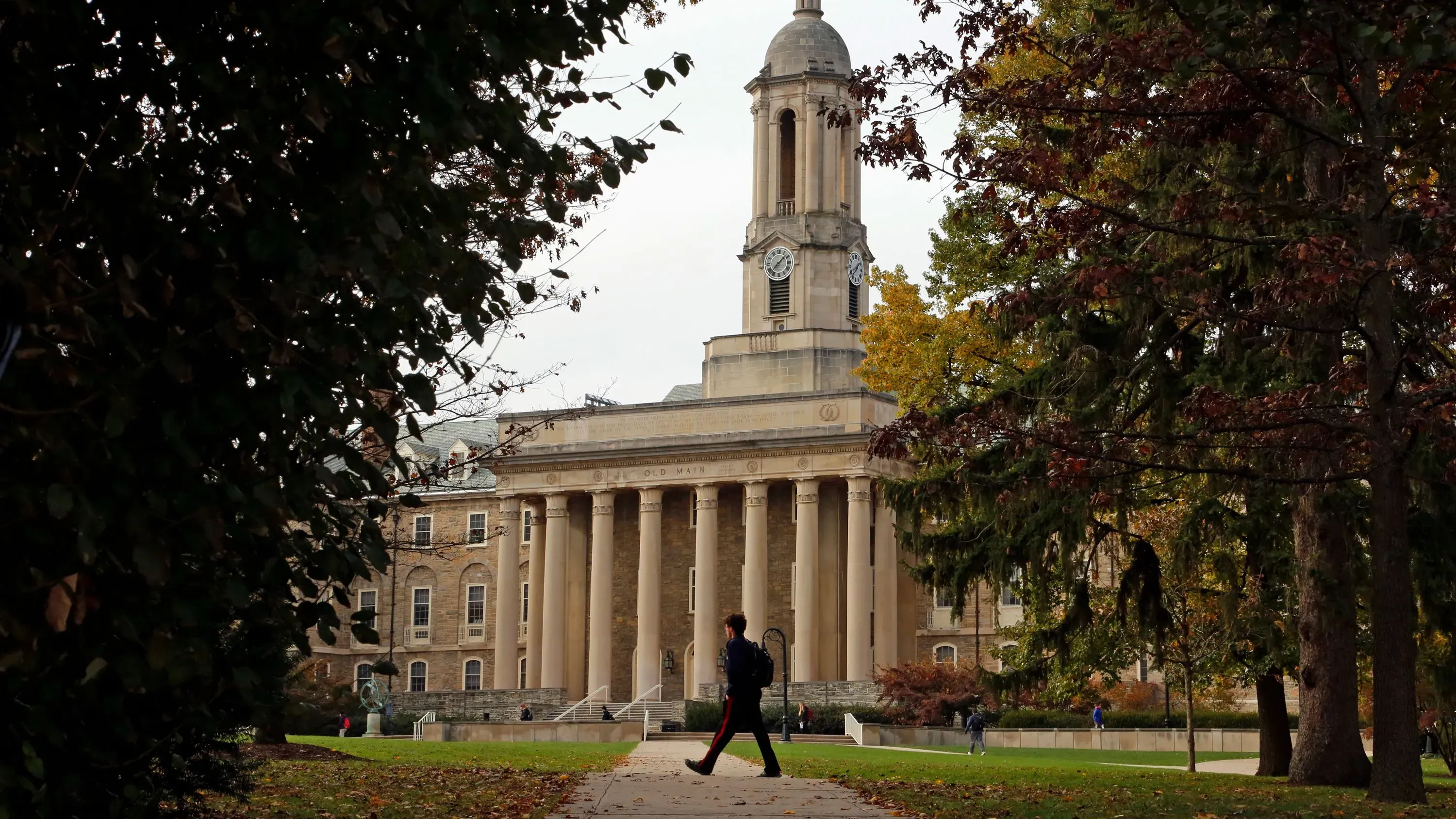 مبنى تعليمي كبير مع أعمدة، حيث يسير طالب في الحرم الجامعي. تعكس الصورة التغييرات في إدارة قروض الطلاب وتأثيرها على التعليم.