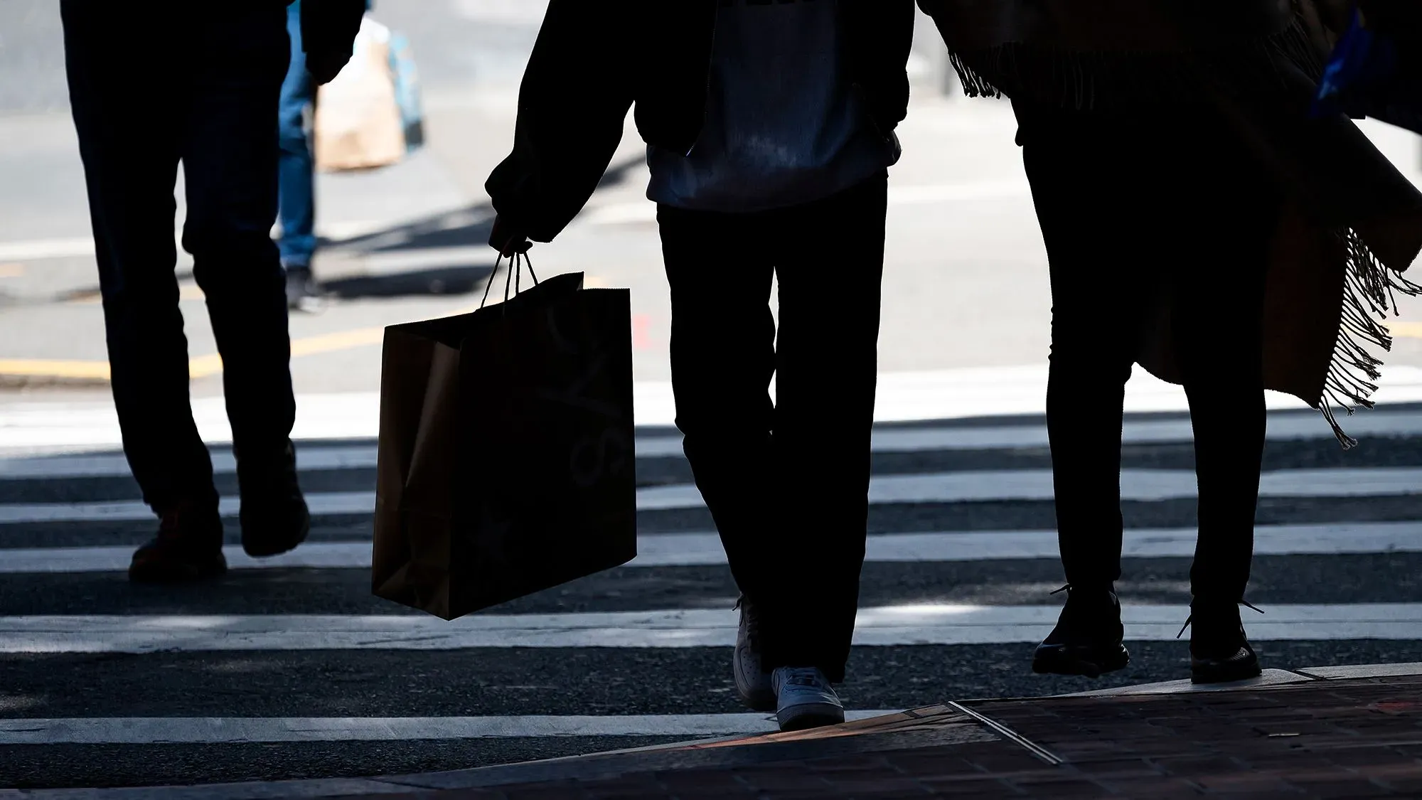 مجموعة من الأشخاص يسيرون عبر ممر مشاة، يحمل أحدهم حقيبة تسوق، مما يعكس النشاط الاقتصادي والإنفاق في ظل المخاوف من الركود.