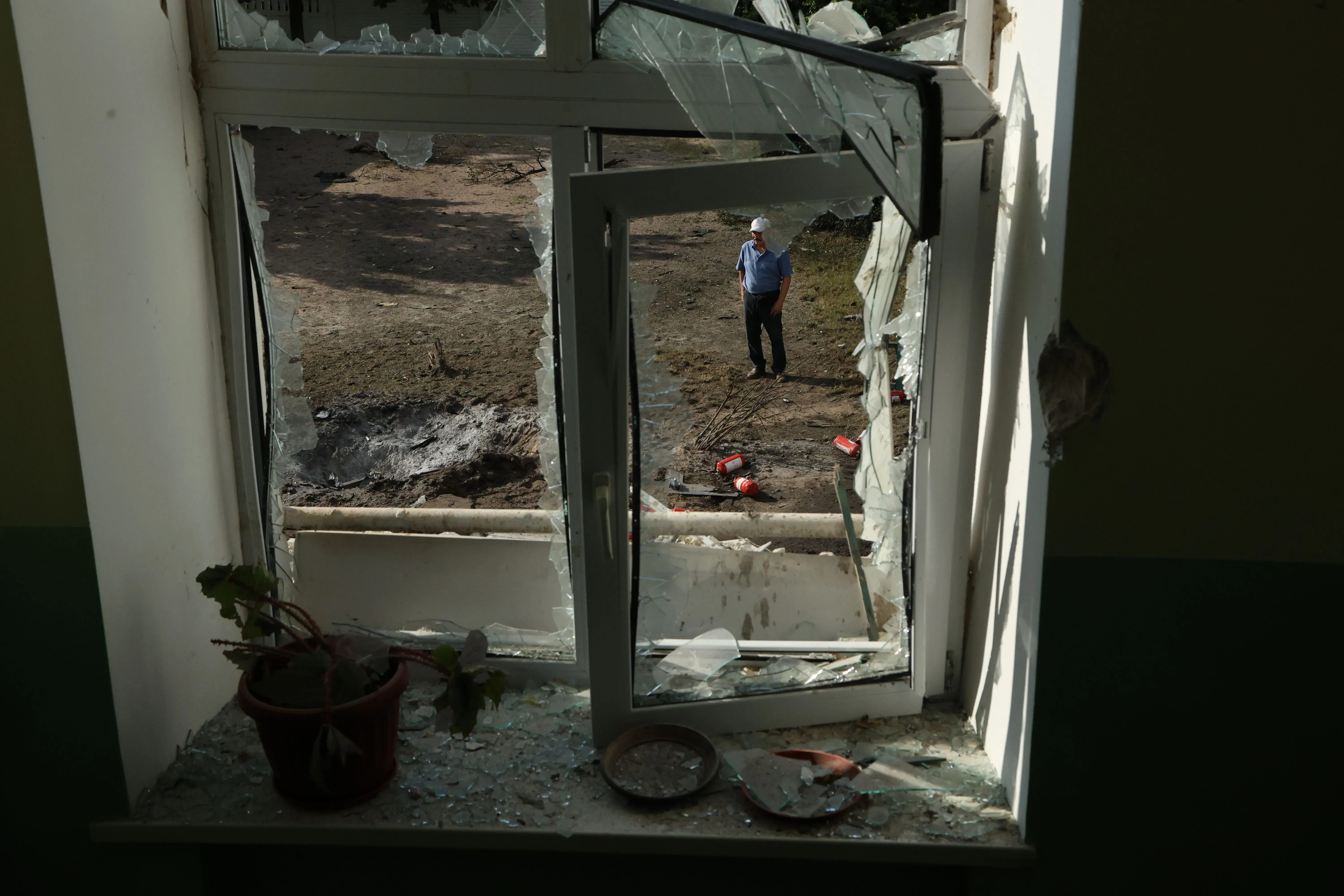 من خلال نافذة مكسورة، يظهر رجل يقف في الخارج بين حطام، مما يعكس آثار الحرب في أوكرانيا وتداعياتها الإنسانية.