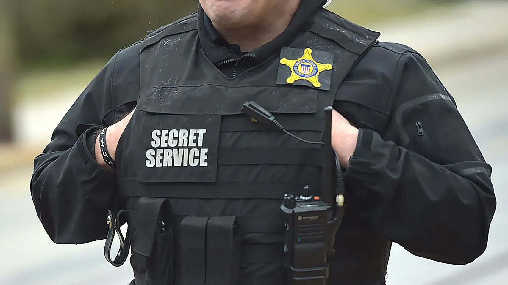 رجل يرتدي سترة واقية تحمل شعار \"الخدمة السرية\"، مع جهاز اتصال، في سياق حماية الرئيس المنتخب دونالد ترامب.