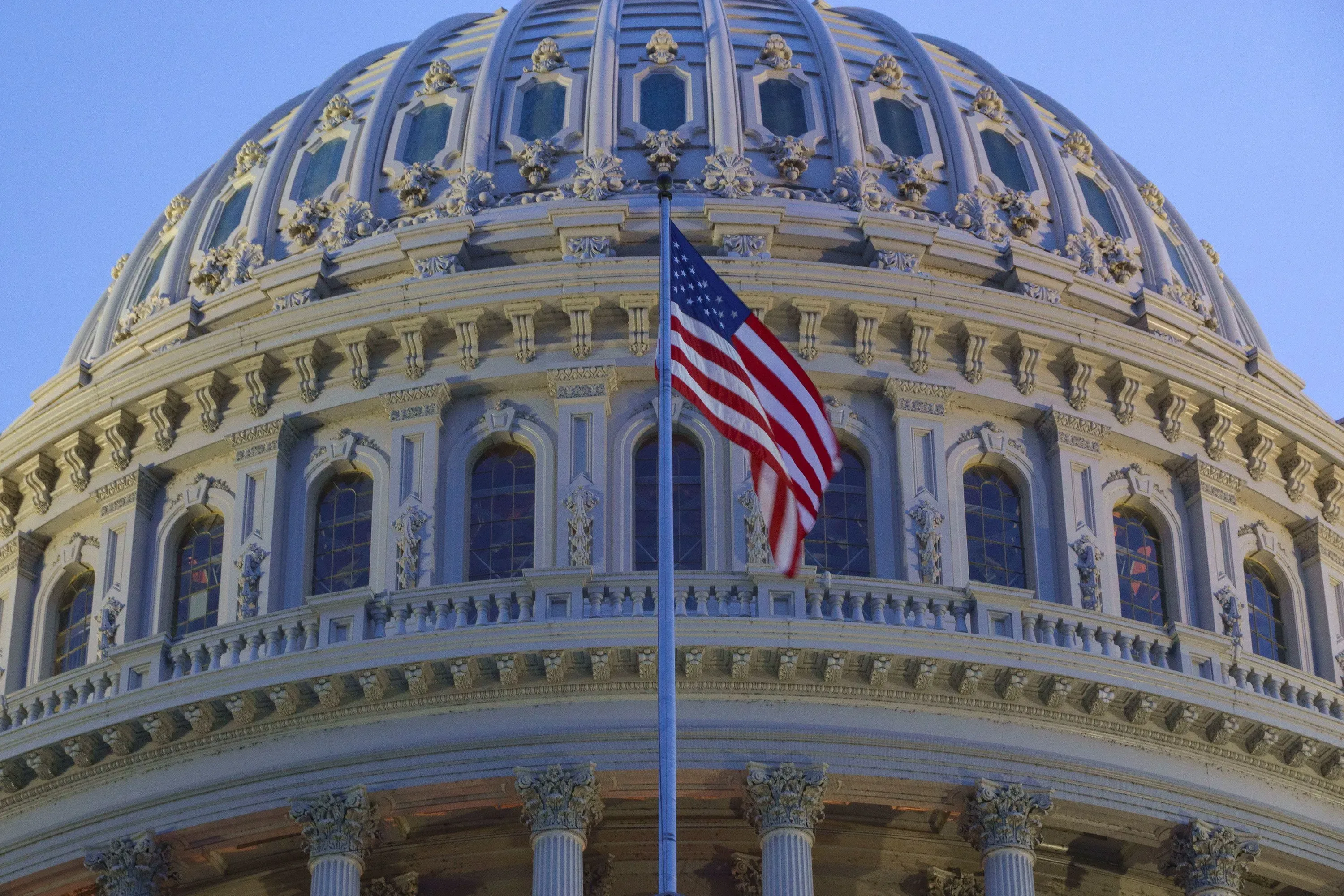 قبة مبنى الكابيتول الأمريكي مع علم الولايات المتحدة يرفرف، تعكس الأجواء السياسية المتوترة في واشنطن.