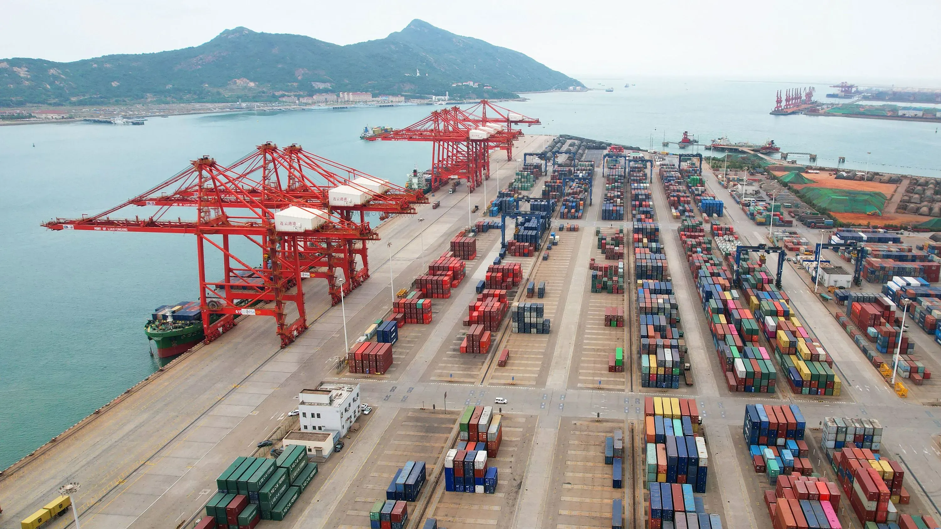 صورة تُظهر ميناءً يحتوي على حاويات شحن ملونة عديدة ورافعات حمراء، تعكس النشاط التجاري واستيراد السلع الصينية.